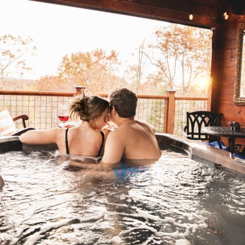Two people relaxing in a hot tub on a covered patio, with autumn trees in the background.