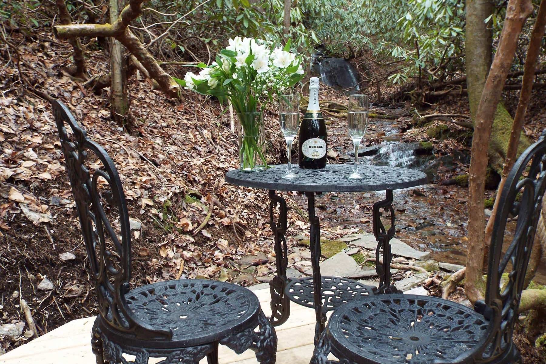 A table with two chairs and a bottle of wine on it in the woods.