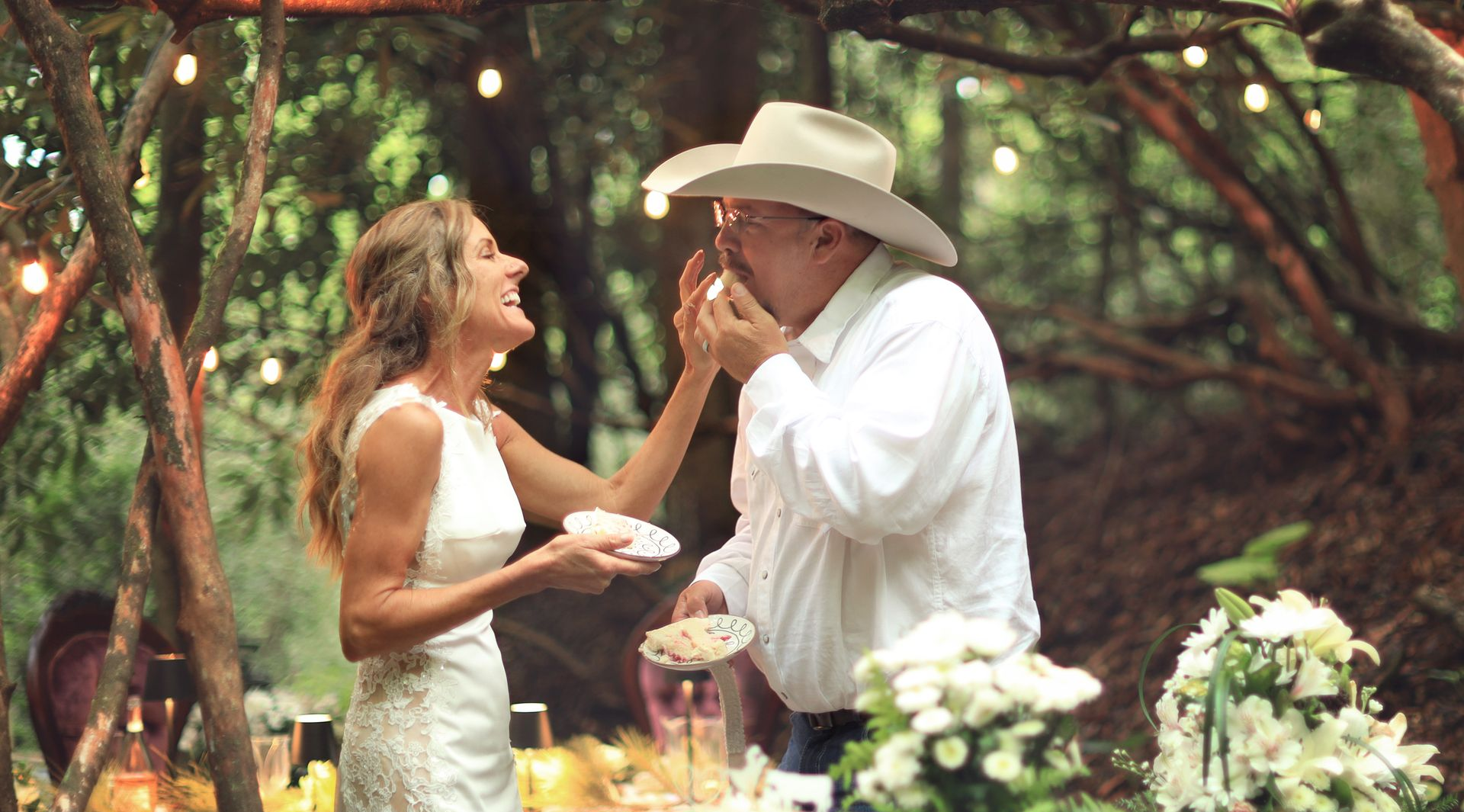 Groom dips bride for a kiss on a wooden bridge in a sunlit forest.