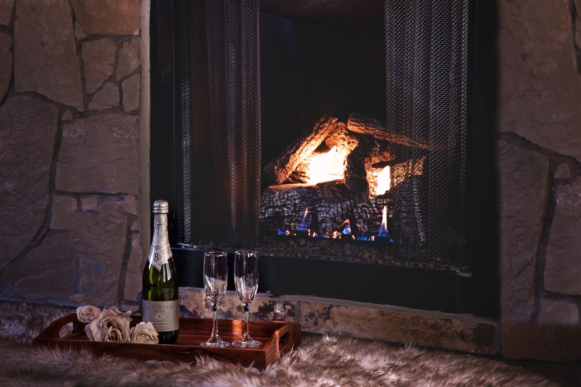 A fireplace with a bottle of champagne and two glasses on a tray
