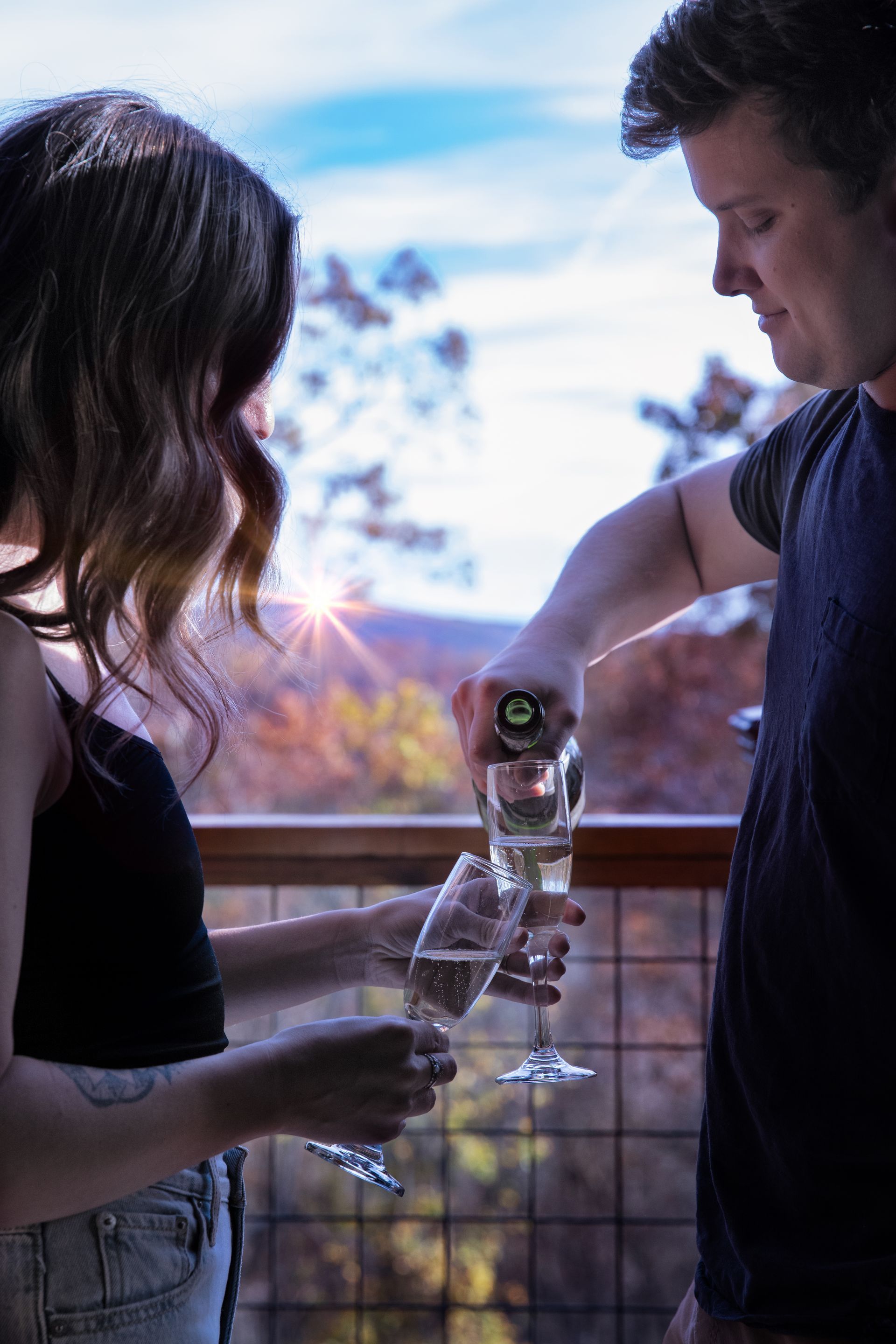Two people toasting champagne on a balcony with mountains in the background