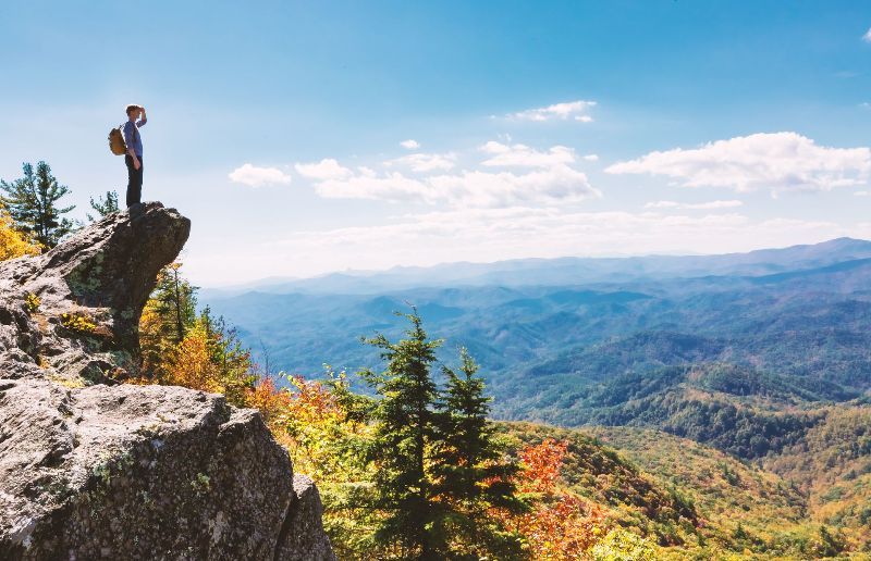A person is standing on top of a rocky cliff overlooking a mountain range.