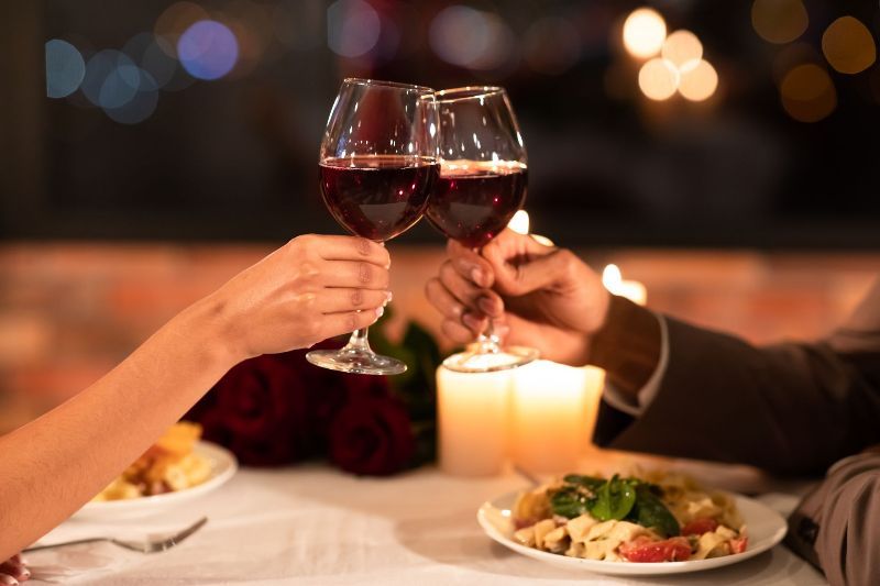 A man and a woman are toasting with wine glasses at a dinner table.
