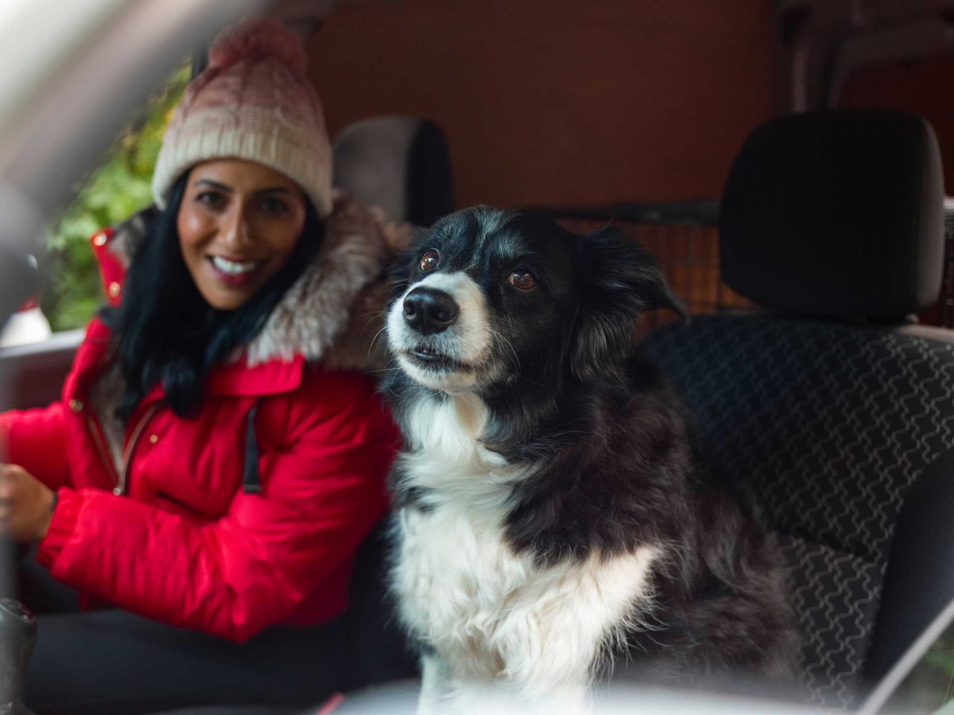 A woman is driving a car with a dog in the back seat.