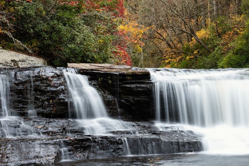 A waterfall is surrounded by trees and rocks in the middle of a forest.