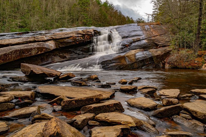 A waterfall is surrounded by rocks and trees in the middle of a forest.