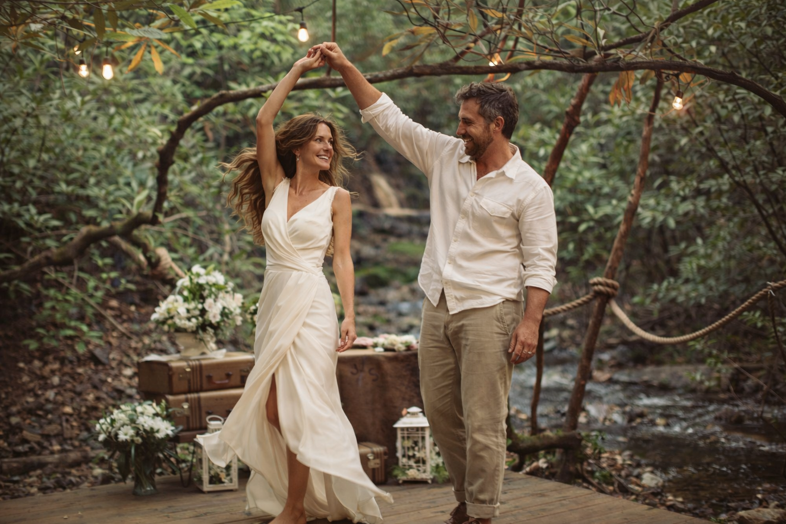 Couple kissing, bride dips backward, groom holds hat, wedding photo in a wooded setting.