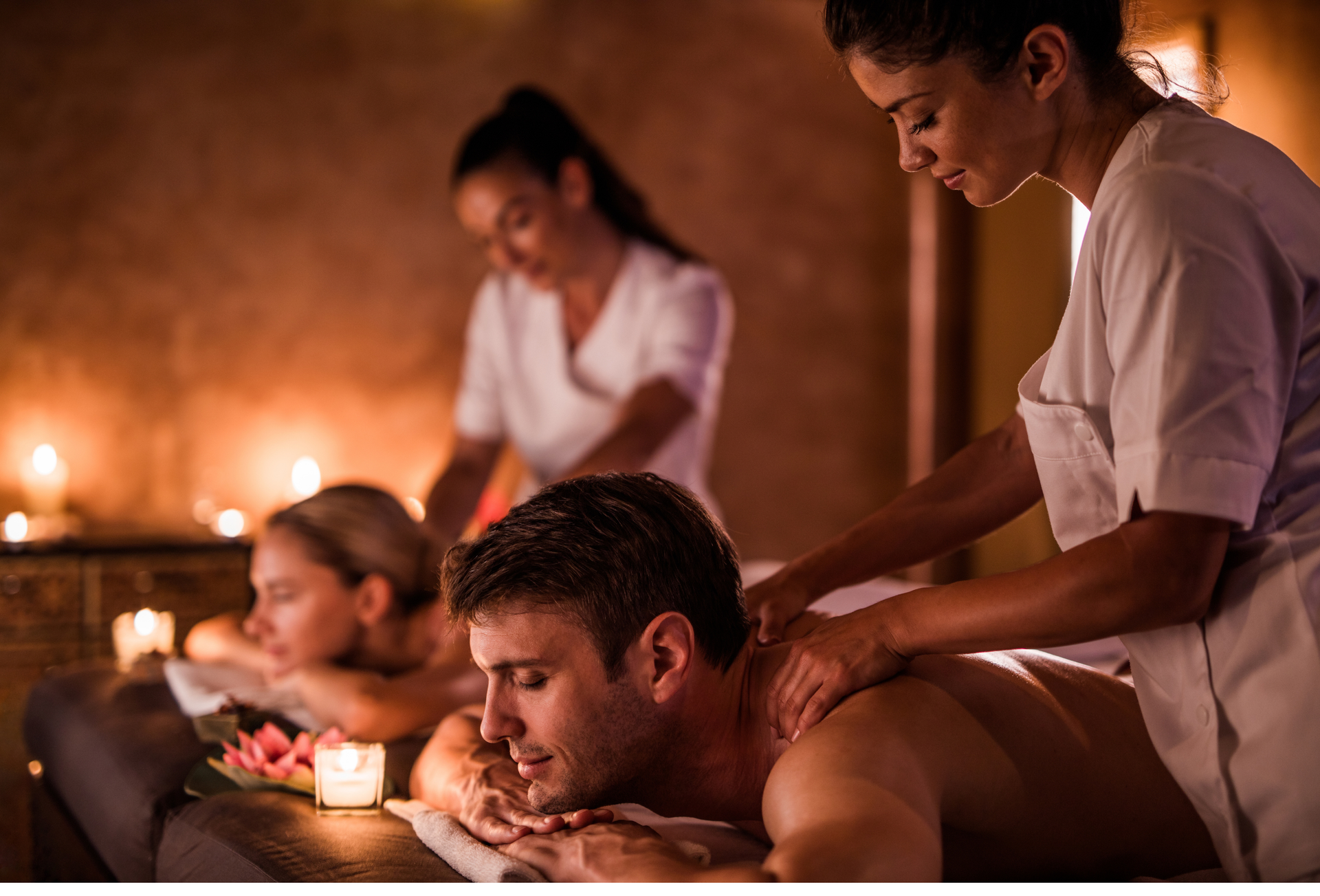 People receiving massages at a spa; masseuses working. Dim lighting, candles.