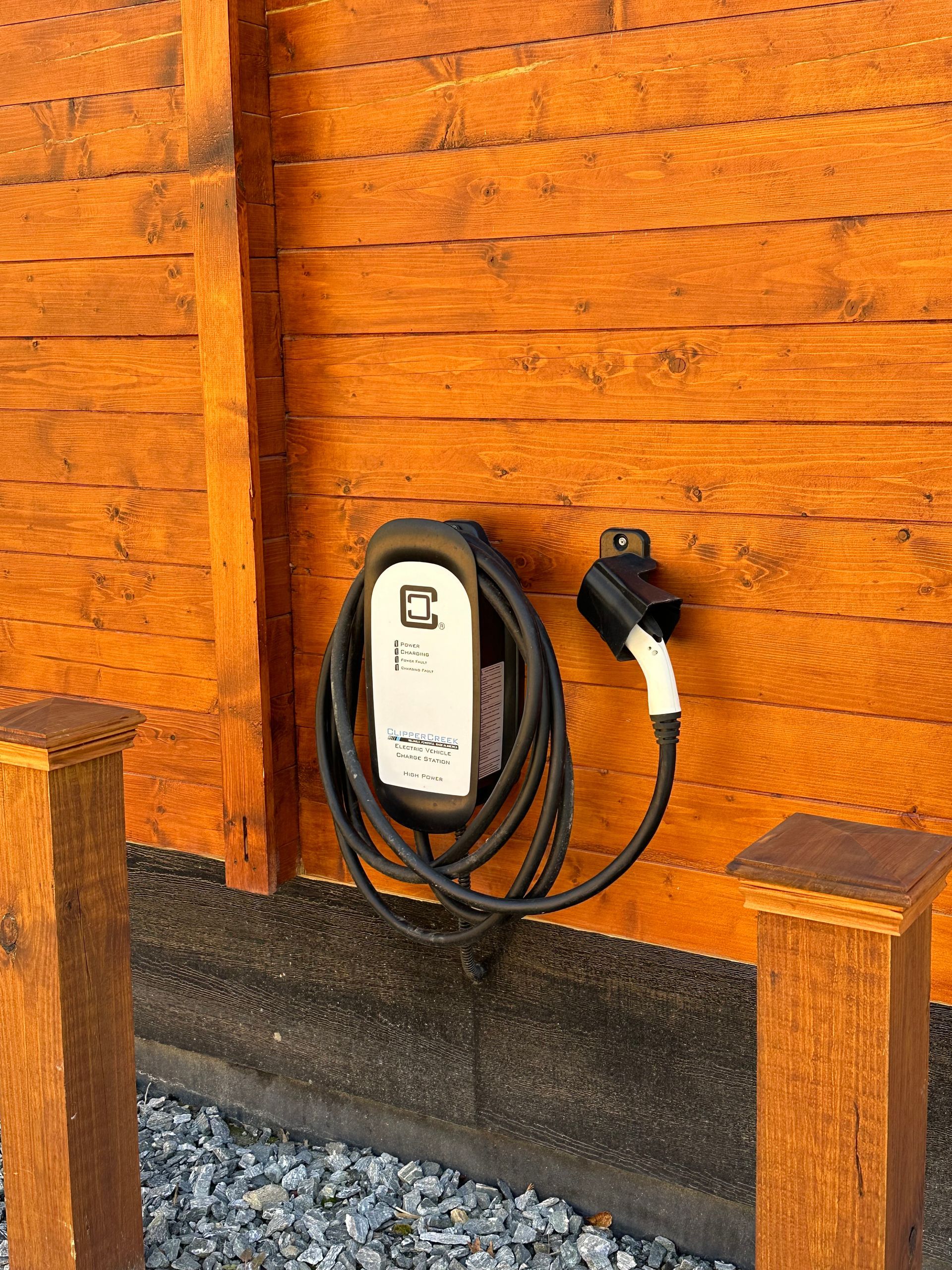 White EV charging unit with coiled cable mounted on an orange wooden wall outdoors
