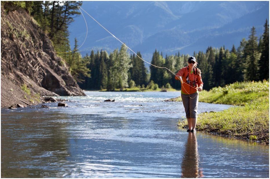 a woman is fishing in a river with mountains in the background .