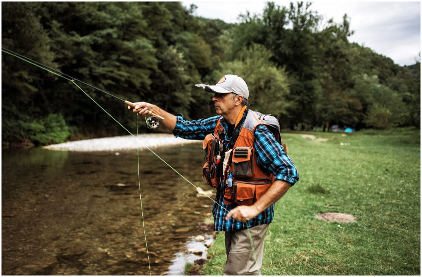 A man is fishing in a river with a fishing rod.