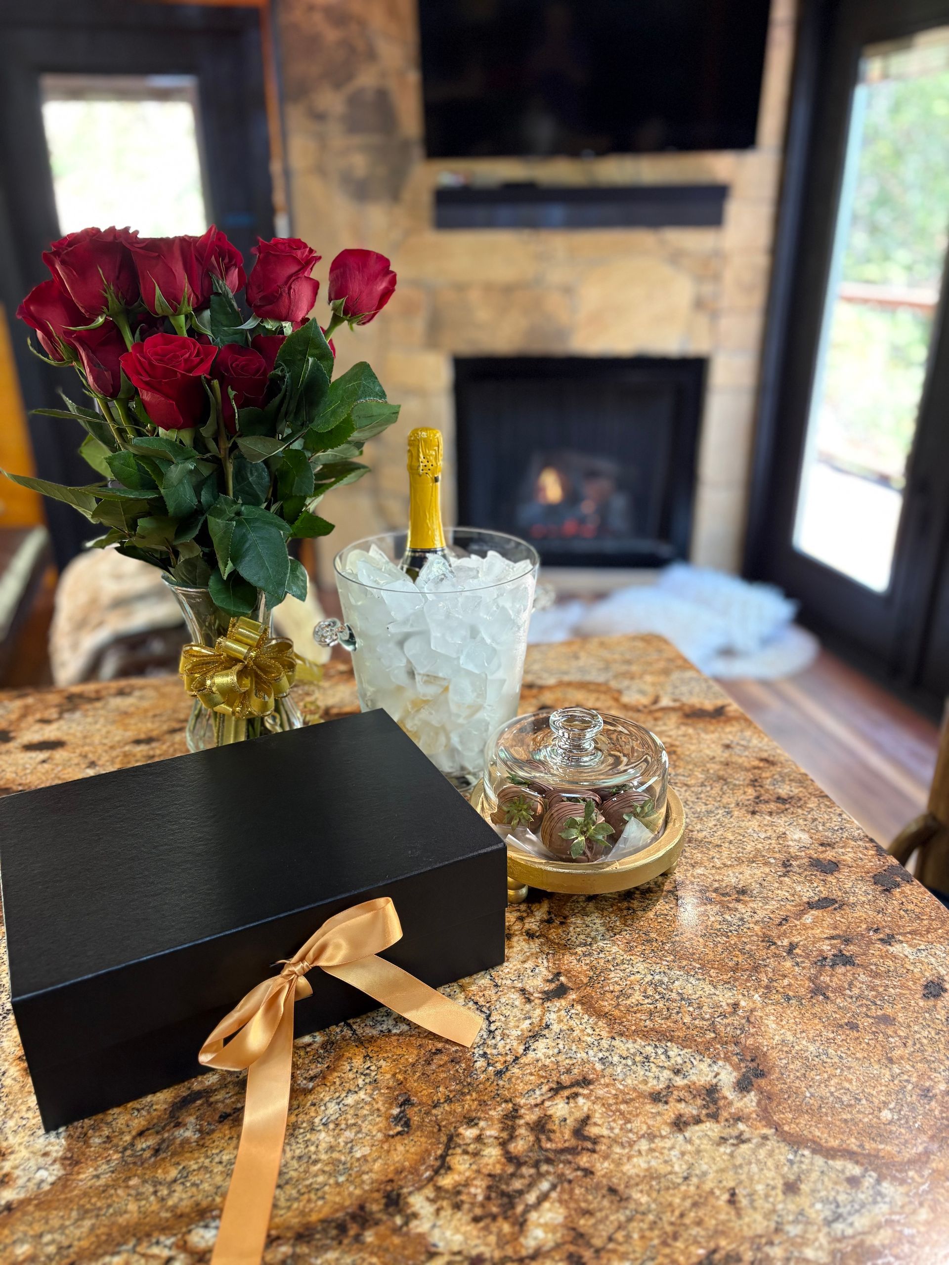 Roses, champagne and a gift box on a marble table in a cozy living room by the fireplace