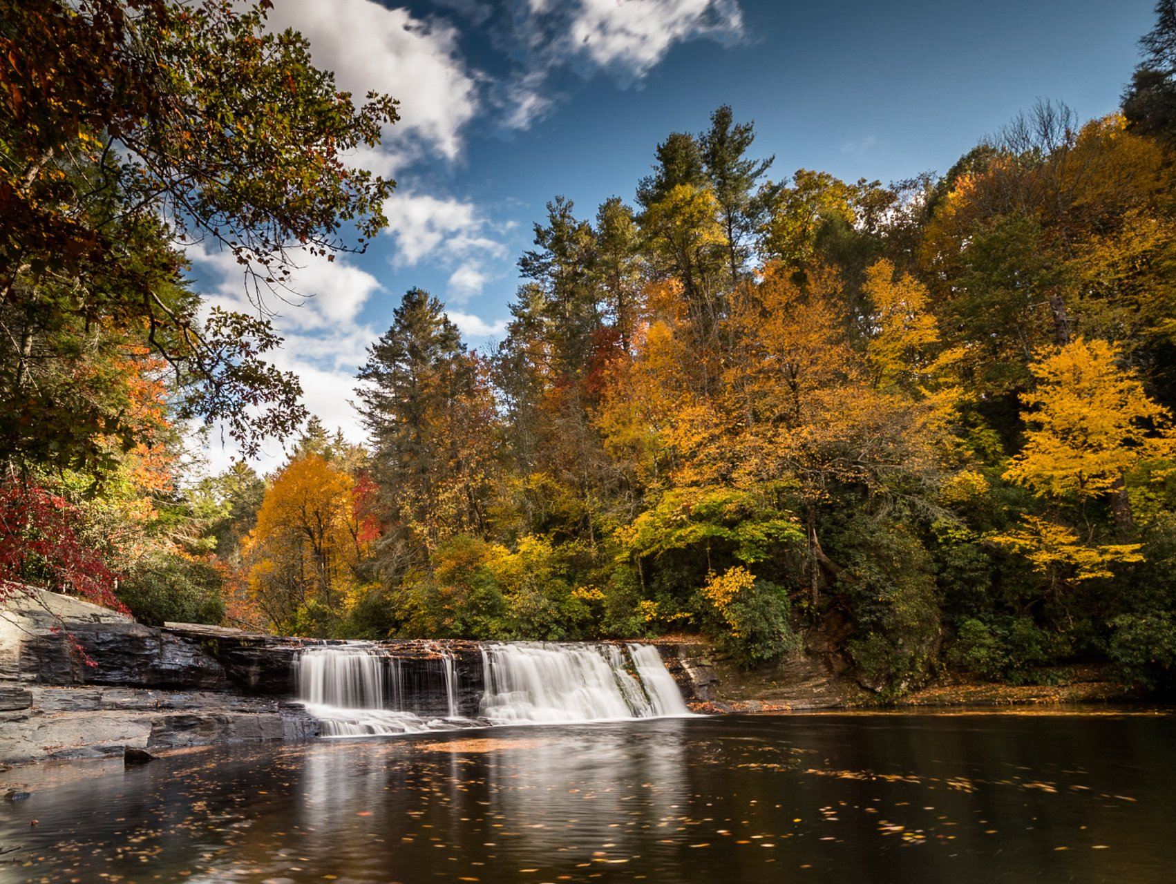a waterfall in the middle of a forest with trees changing colors