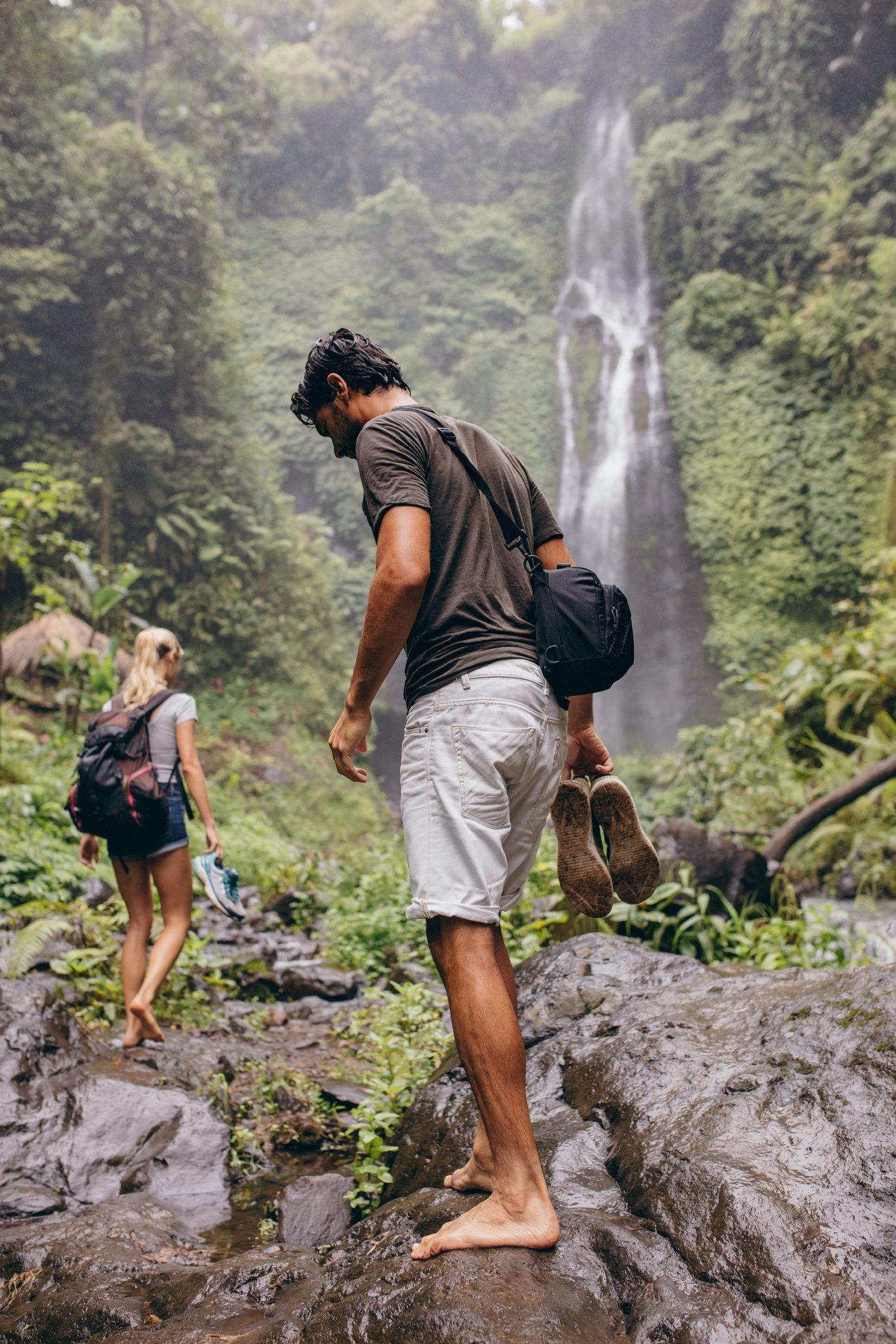 a man and a woman are hiking in the woods near a waterfall .