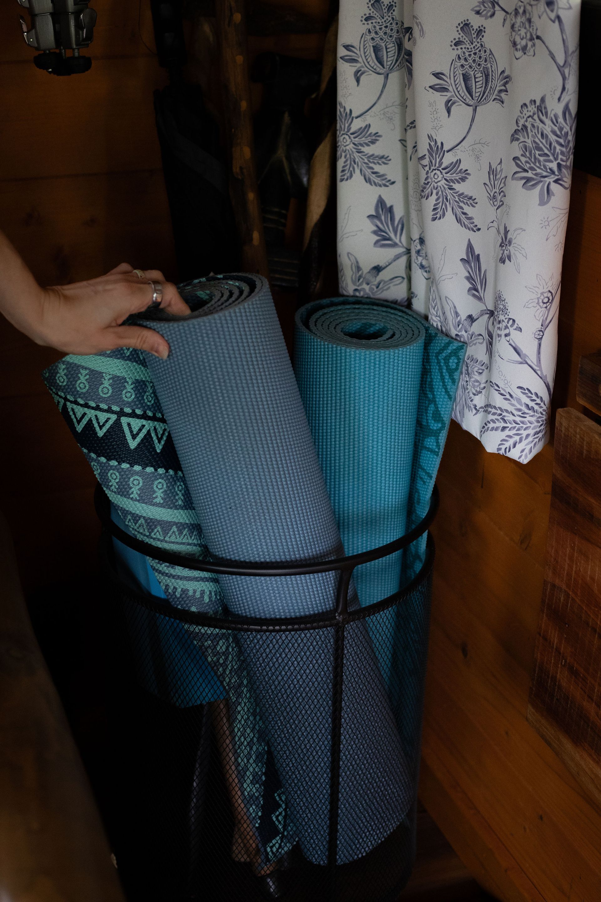 Hand placing rolled blue yoga mats into a wire storage basket in a wooden room