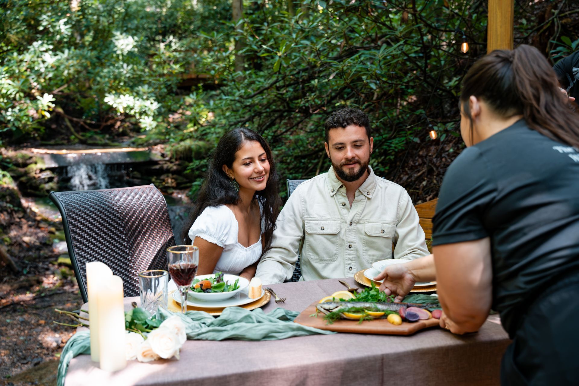 A table with two chairs and a bottle of wine on it in the woods.