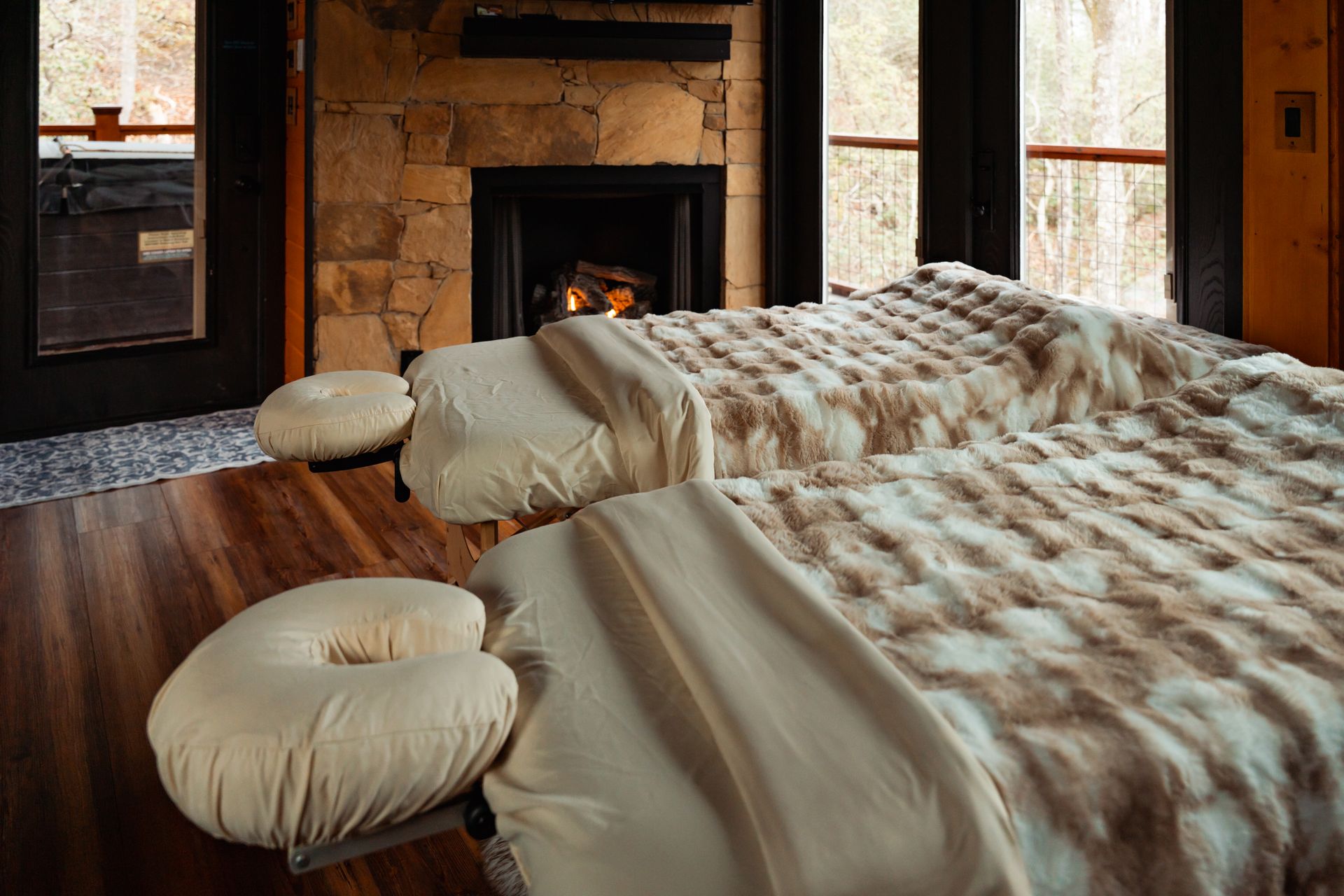Cozy bedroom with two beige beds, round floor cushions, and a stone fireplace by large windows