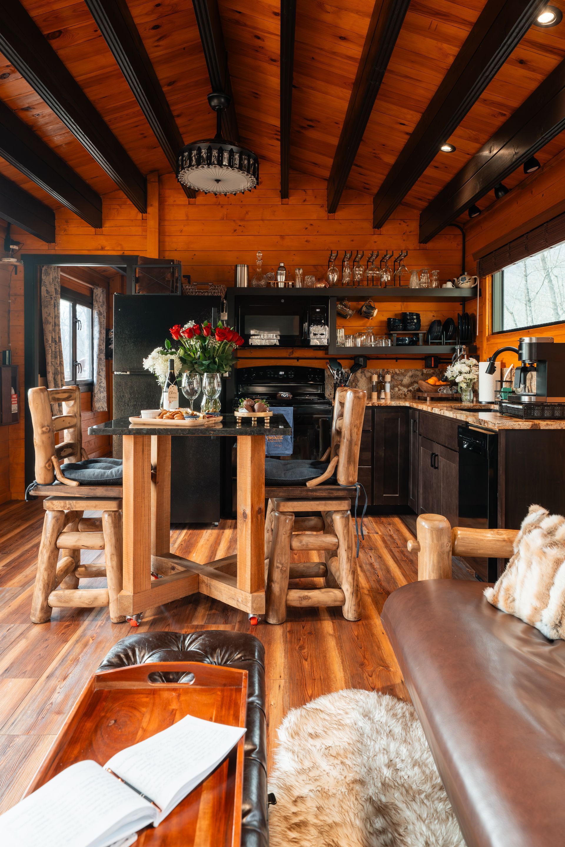 Rustic kitchen and living space with wood beams, leather sofa, and a small dining table with flowers