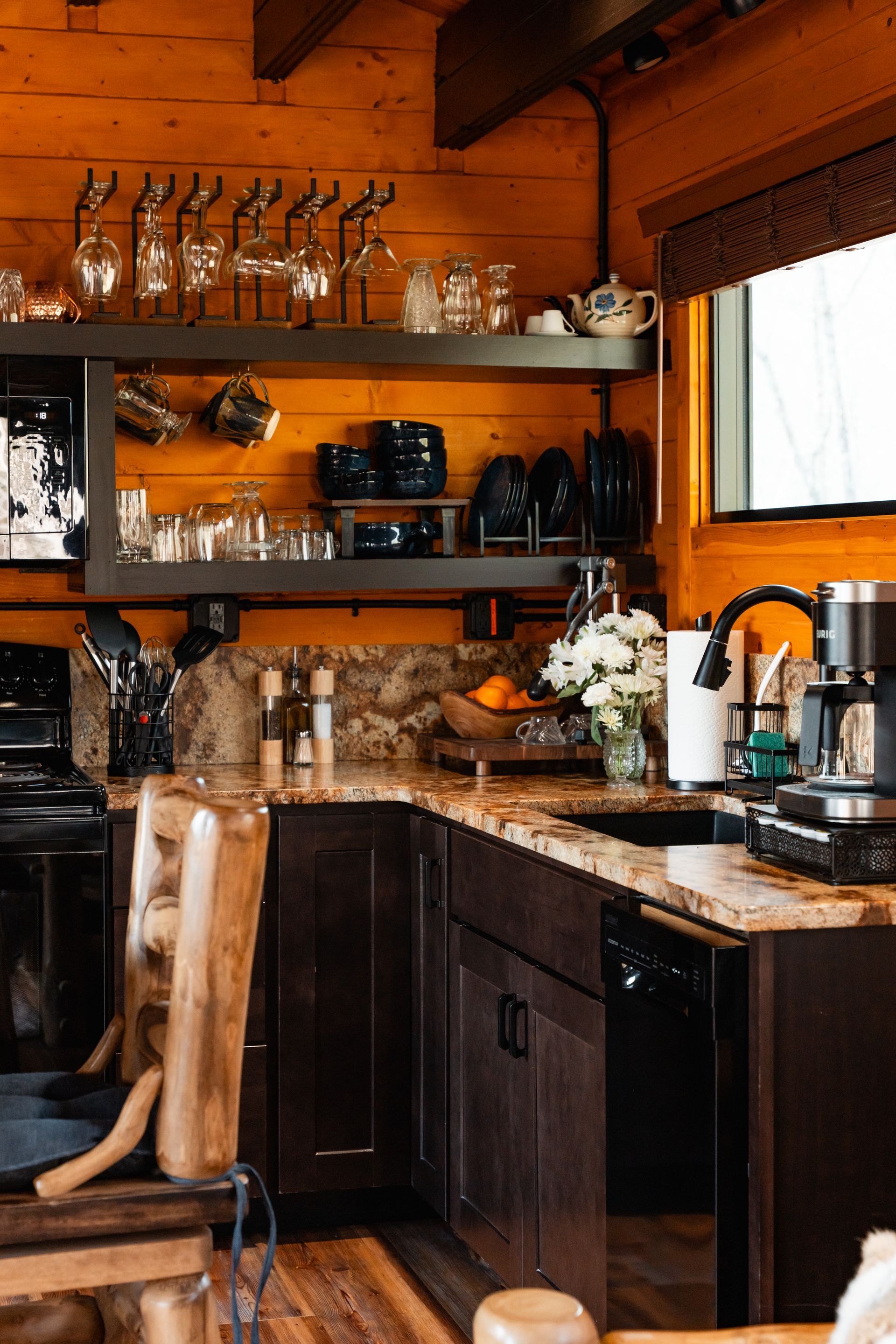Cozy wooden kitchen with black cabinets, open shelves, dishes, coffee maker, and a window by the sink