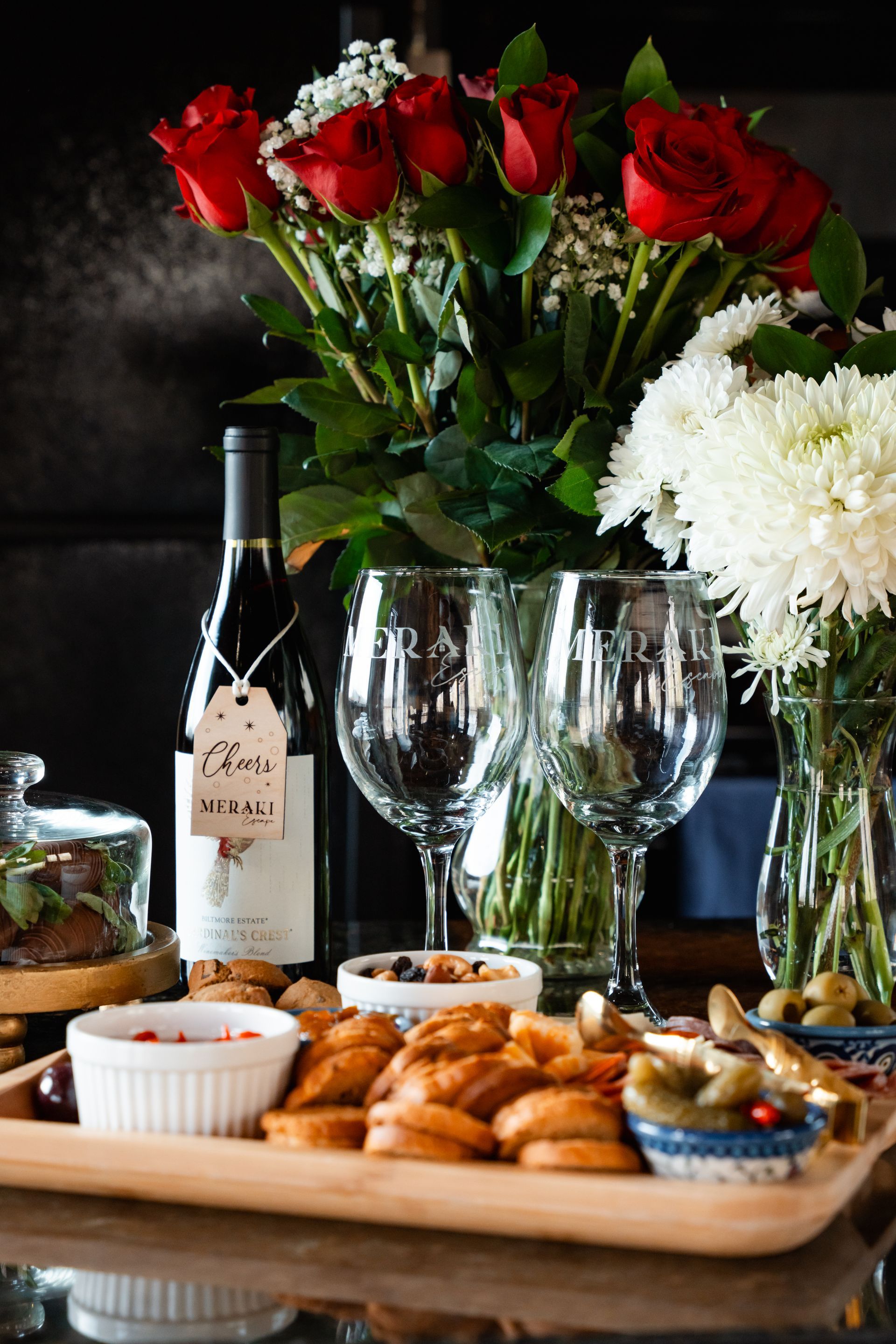 Wine, red roses, and white flowers arranged on a table with appetizers and glassware