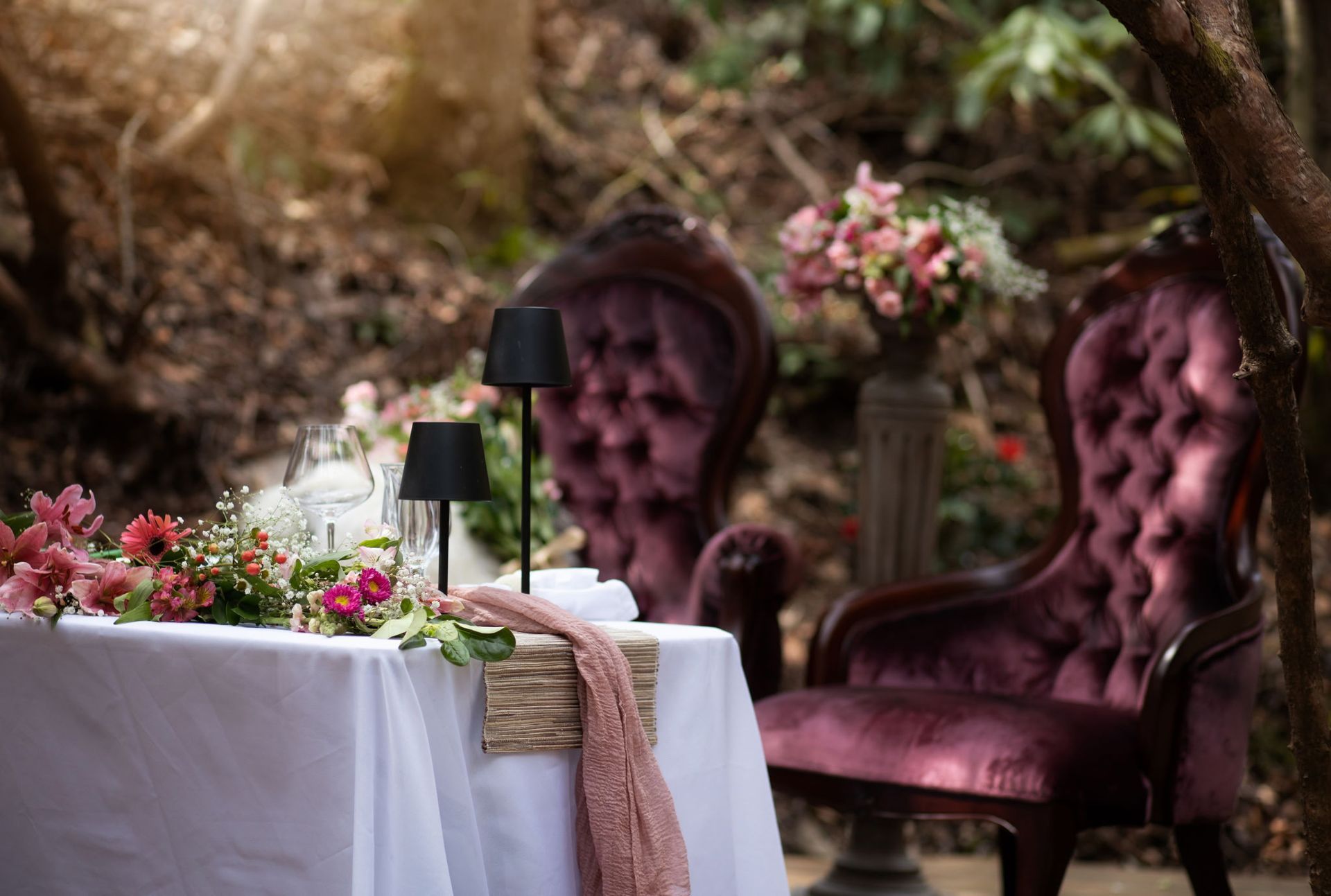 A table with flowers and a chair in the woods.