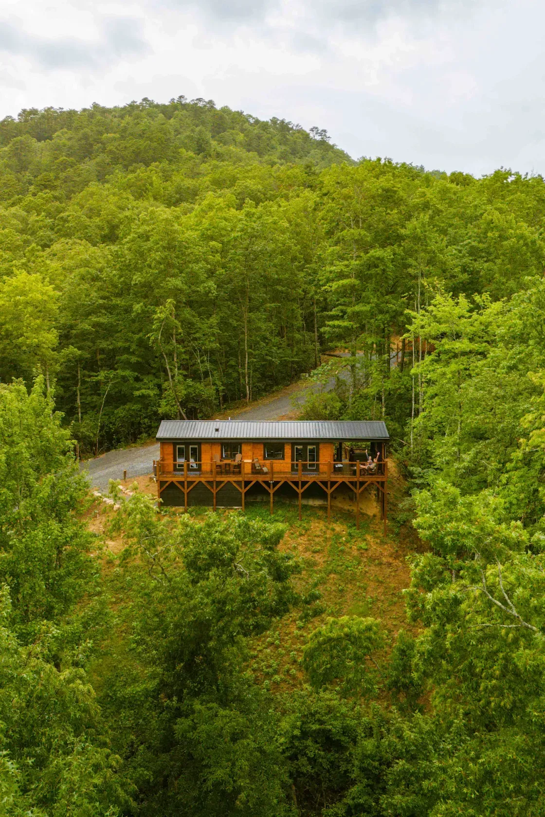 Wooden cabin on a hillside surrounded by lush green forest and hills