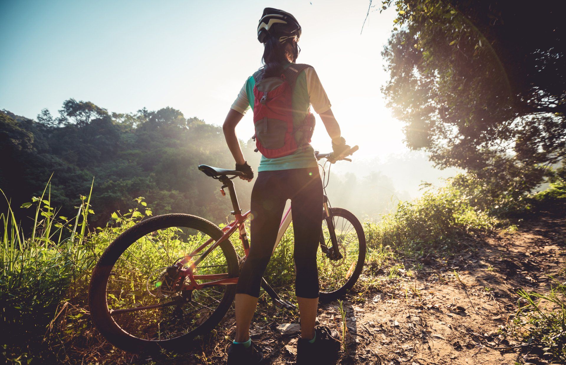 a woman is standing next to a bicycle on a dirt road .
