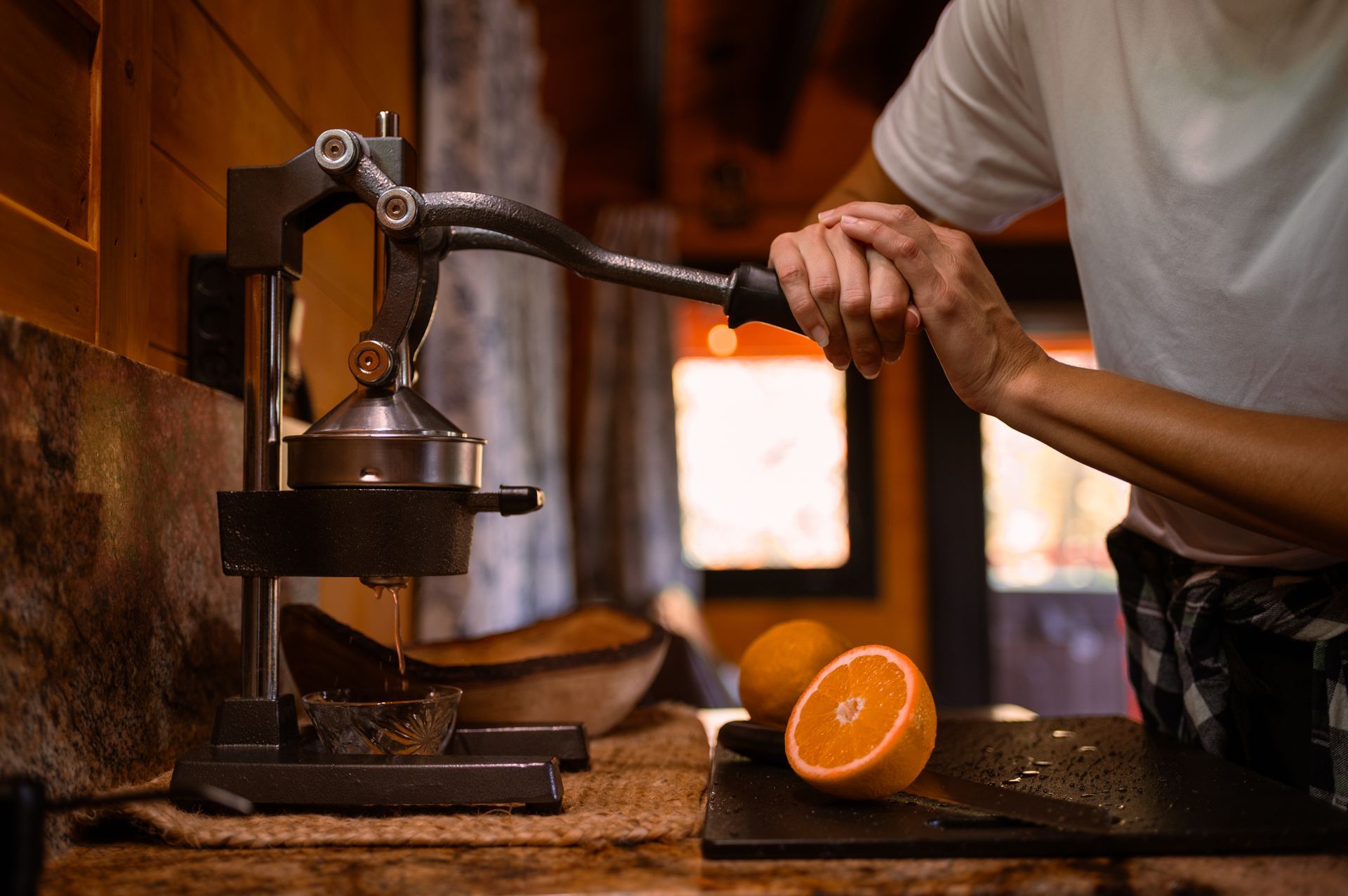 Hand pressing a metal press to squeeze an orange on a rustic wooden table, with cut fruit nearby
