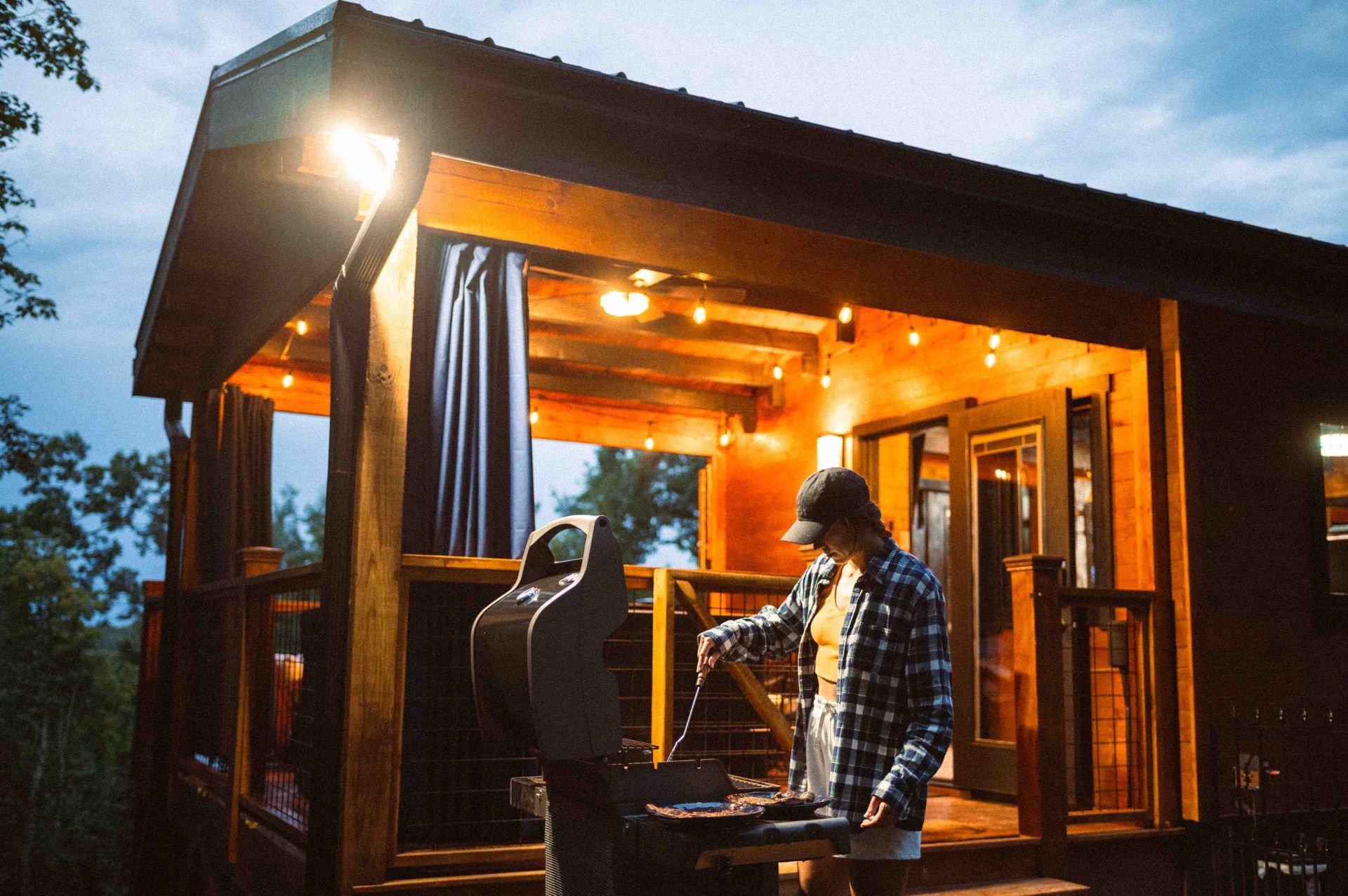 Person grilling at a warmly lit wooden cabin deck at dusk