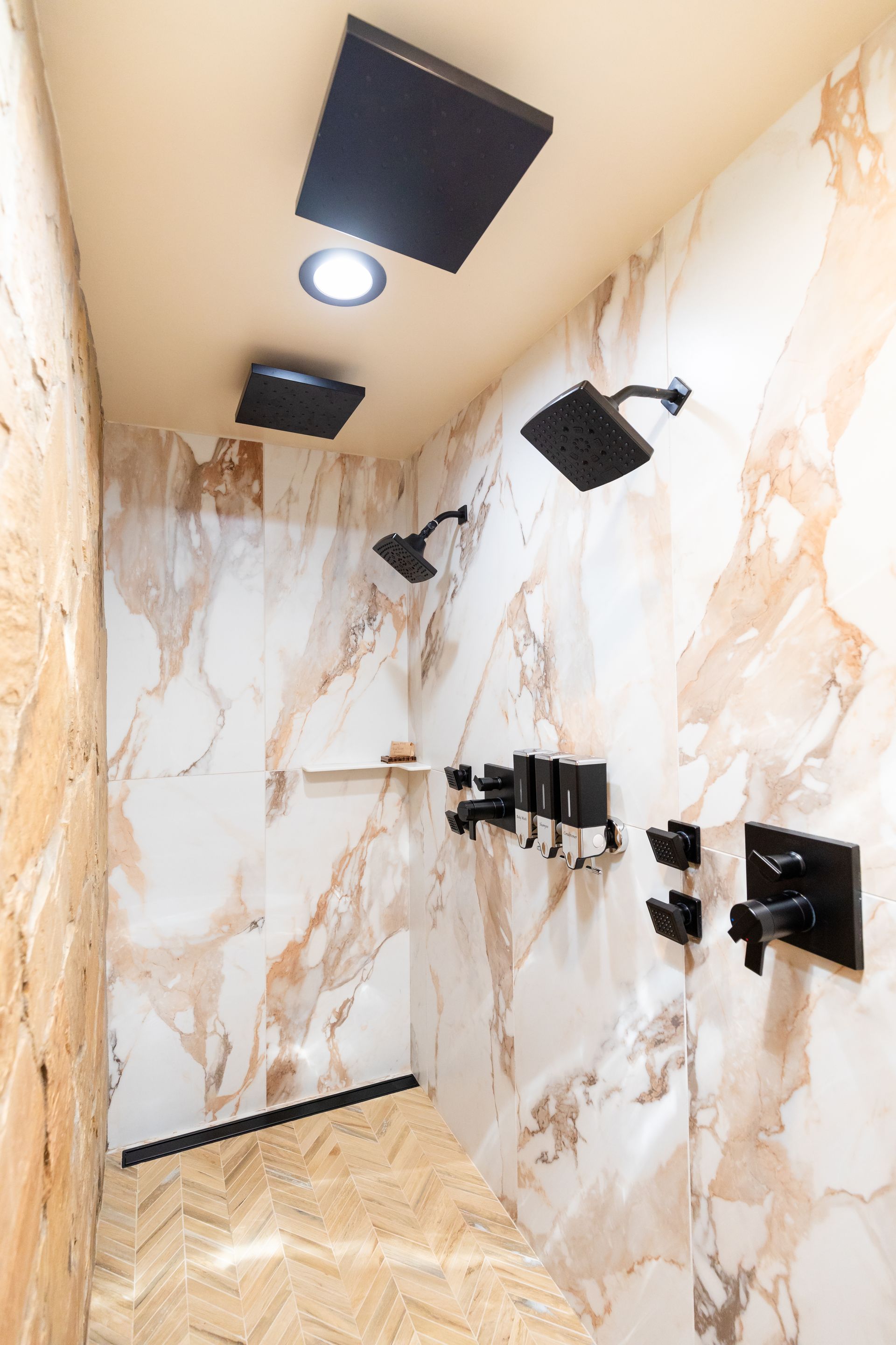 Marble-tiled shower room with black fixtures and ceiling shower heads
