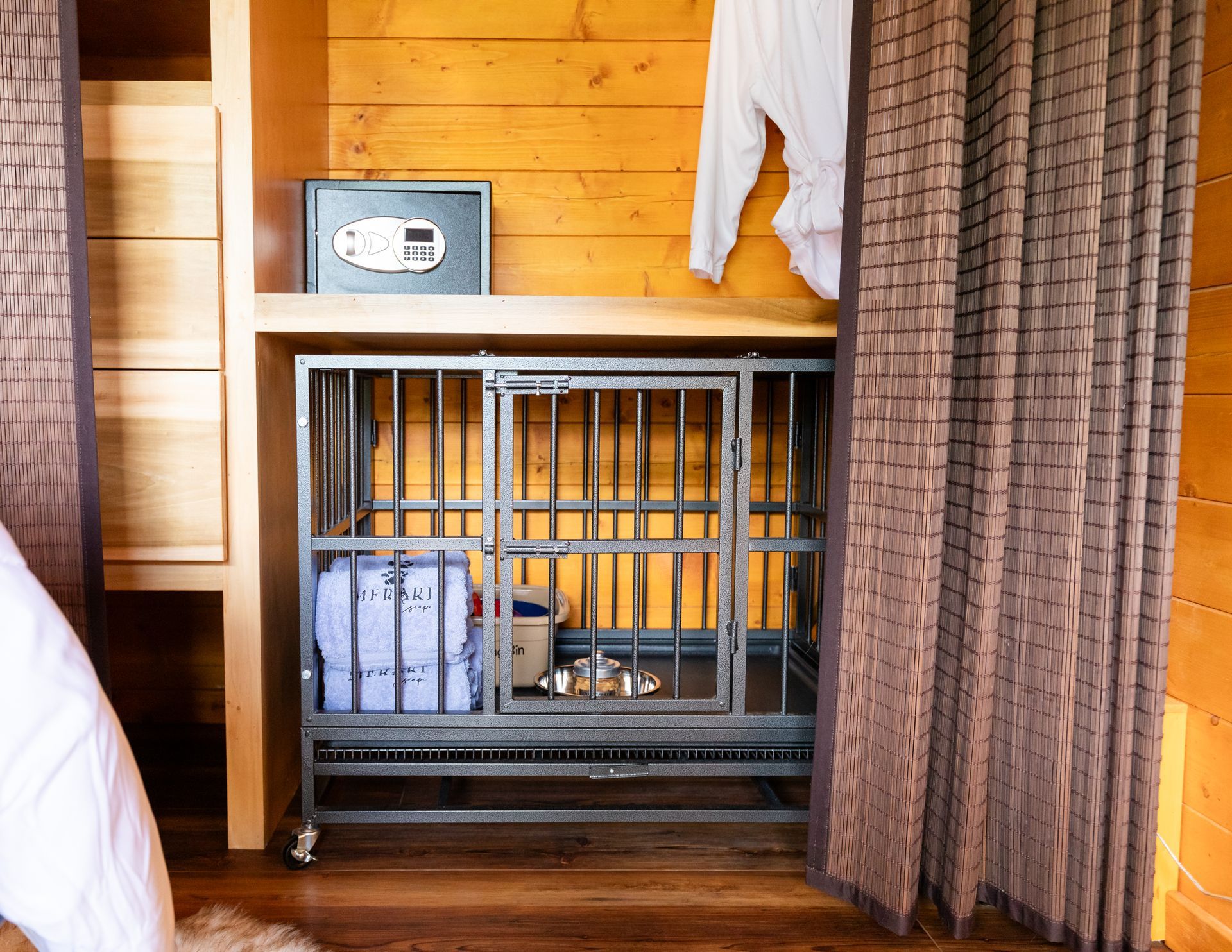 Small metal dog crate in a wood-paneled room with a curtain partially covering it