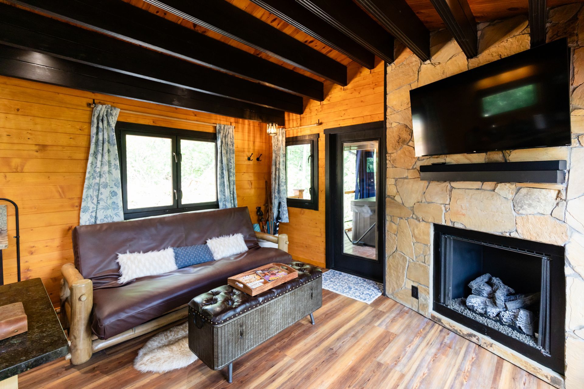 Cozy rustic living room with exposed beams, leather sofa, fireplace, and wall-mounted TV