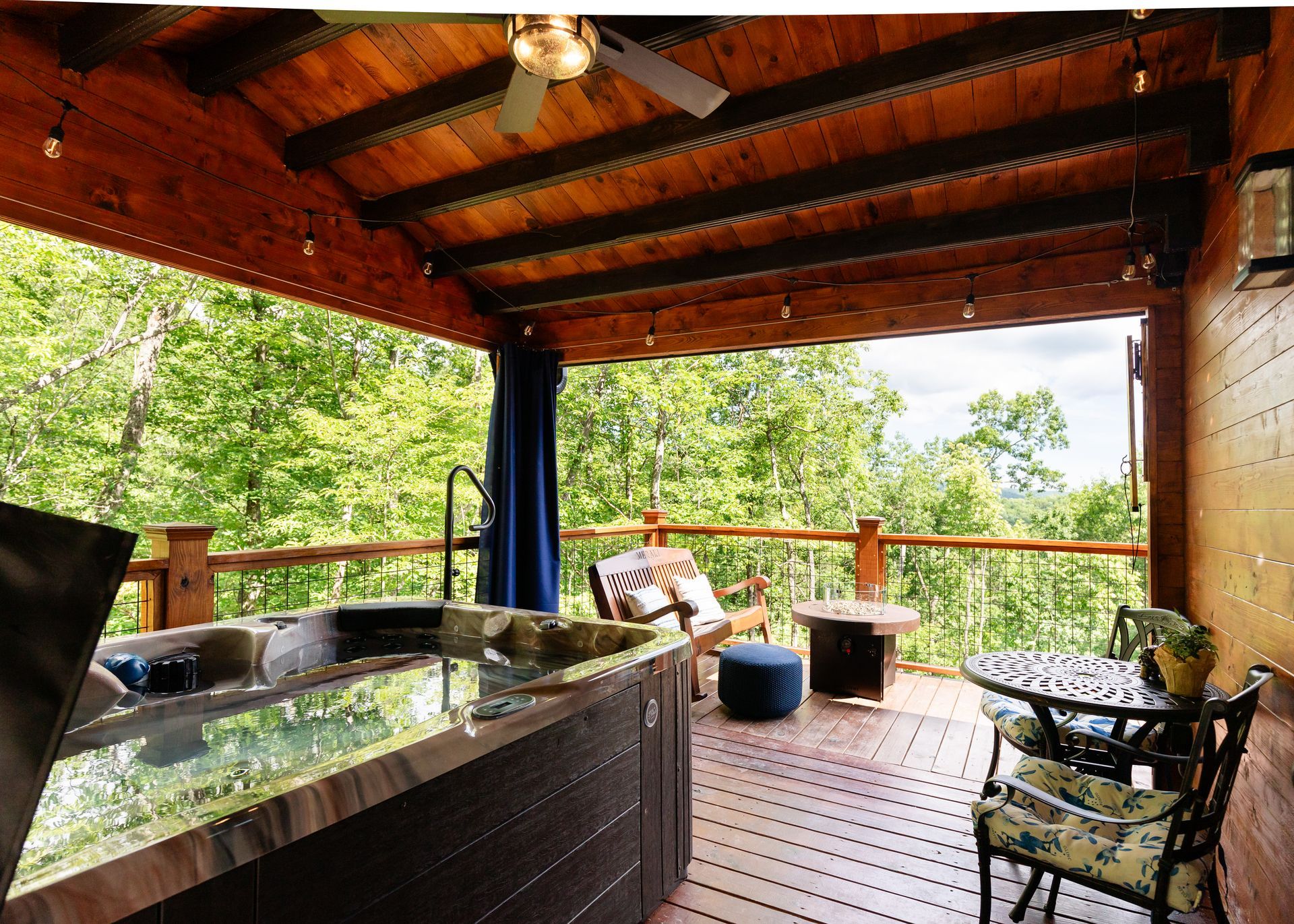 Covered wooden deck with hot tub, chairs, and forest view