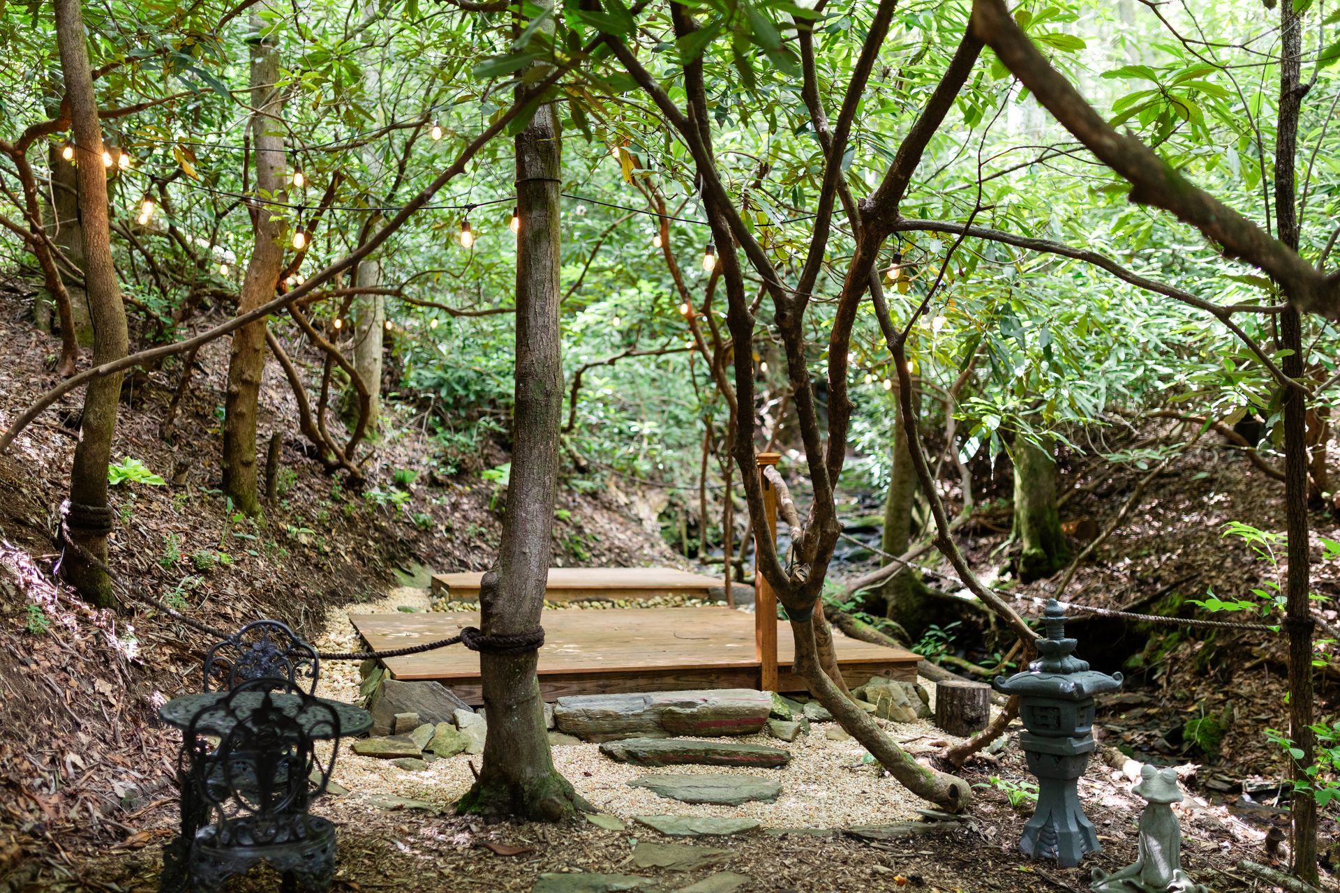 Wooded garden with stone steps, a wooden bench, and lanterns under leafy trees