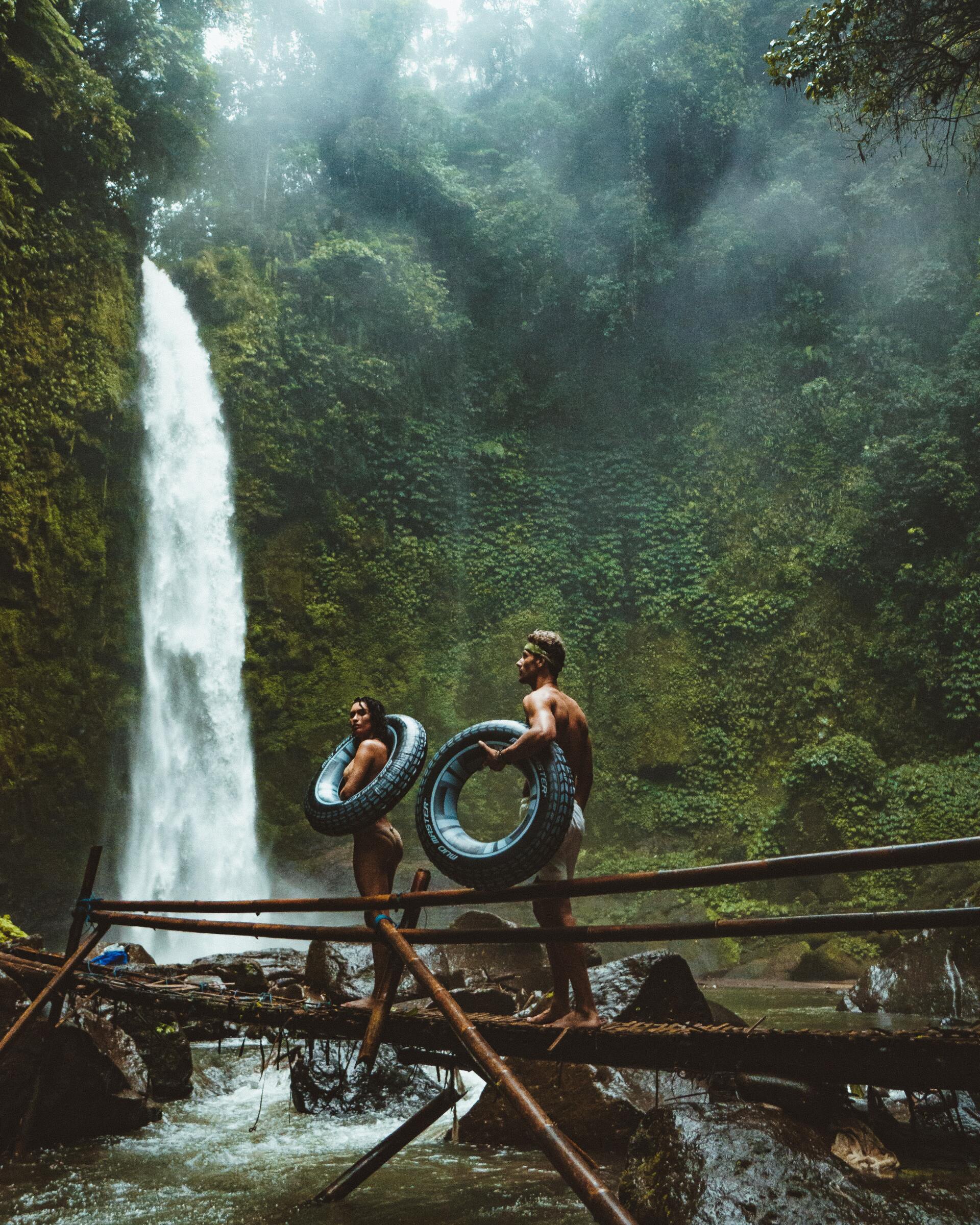 a man and a woman are standing on a bridge in front of a waterfall .