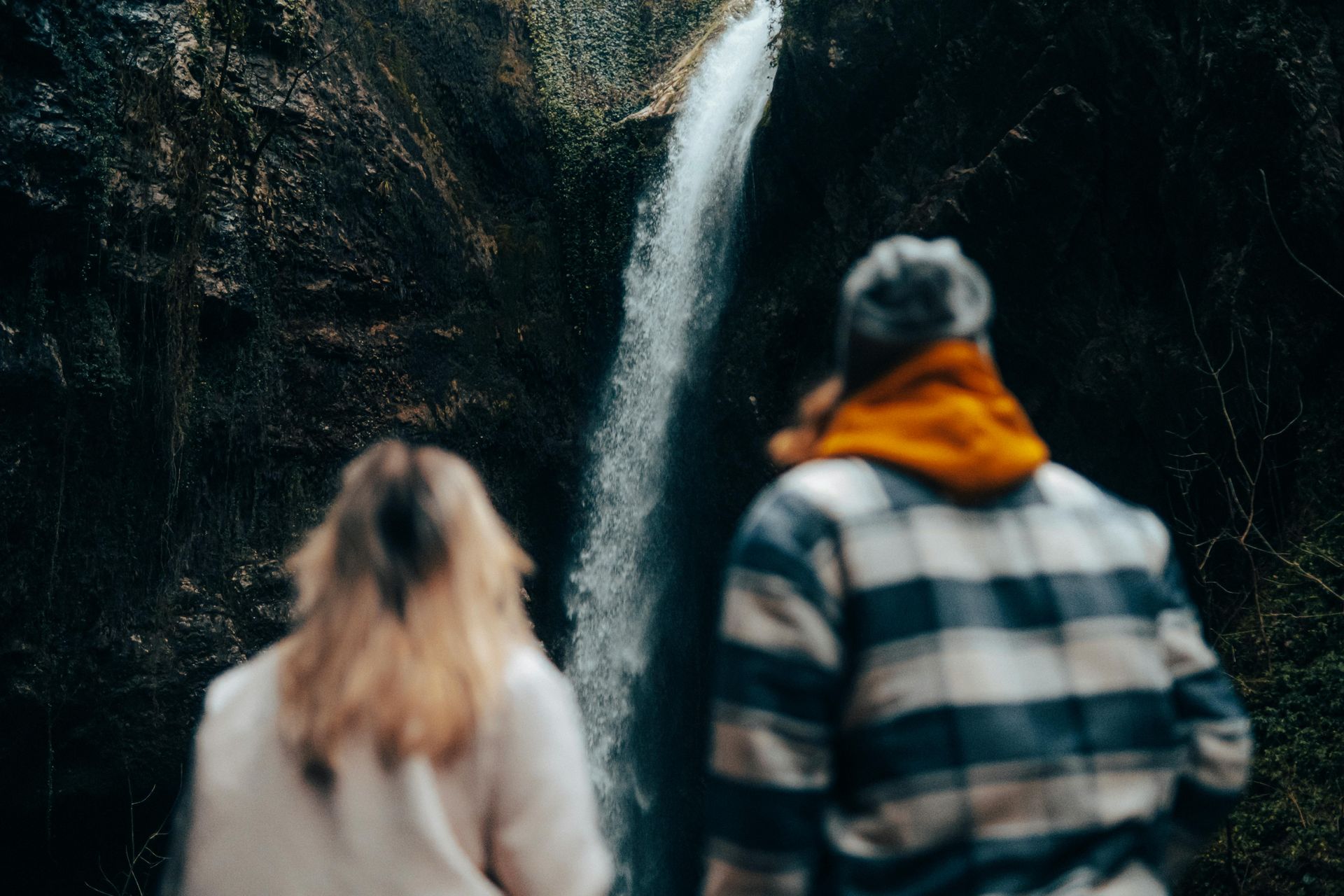 A man and a woman are standing in front of a waterfall.