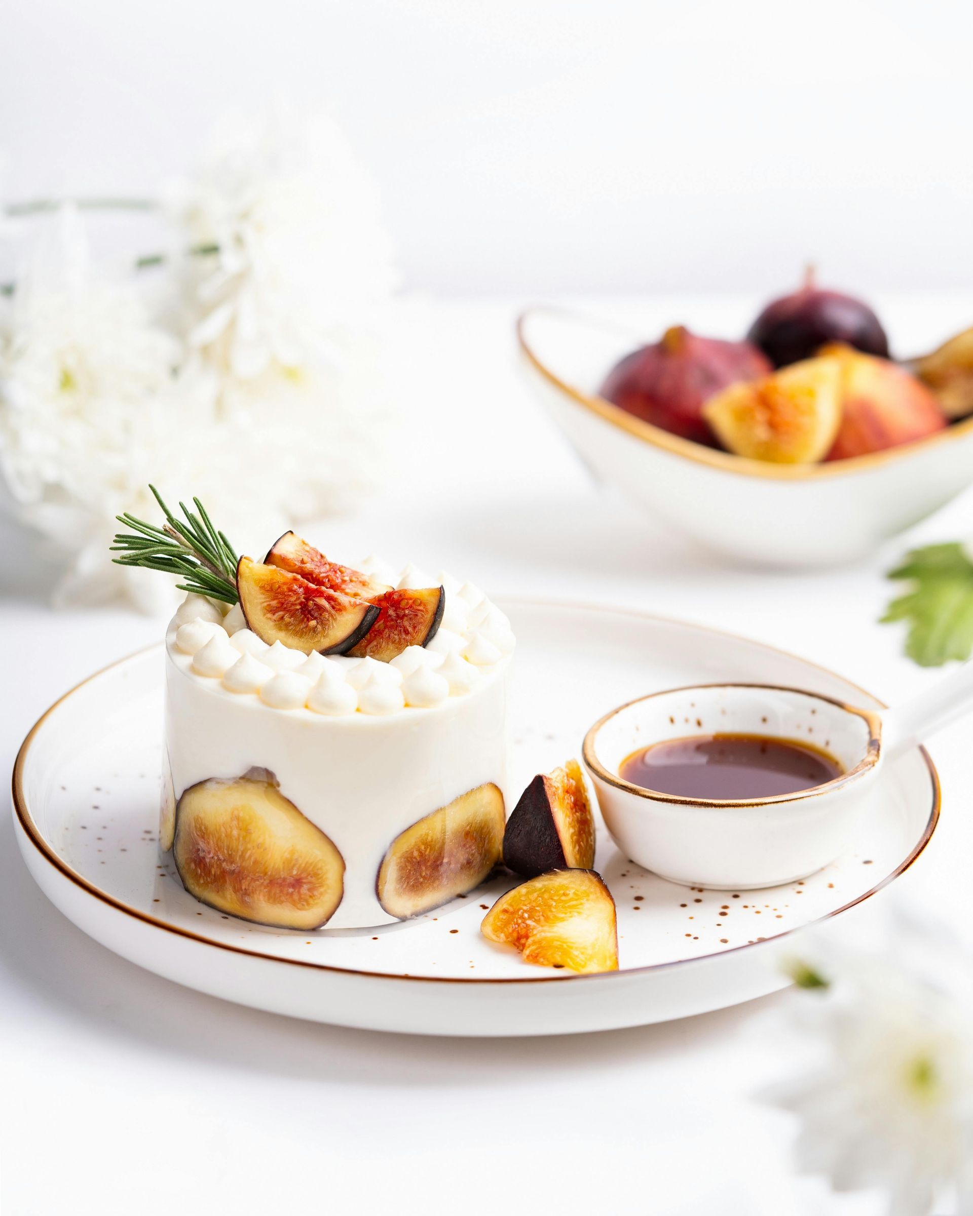 Cake decorated with figs and rosemary, served with sauce and figs in a bowl.