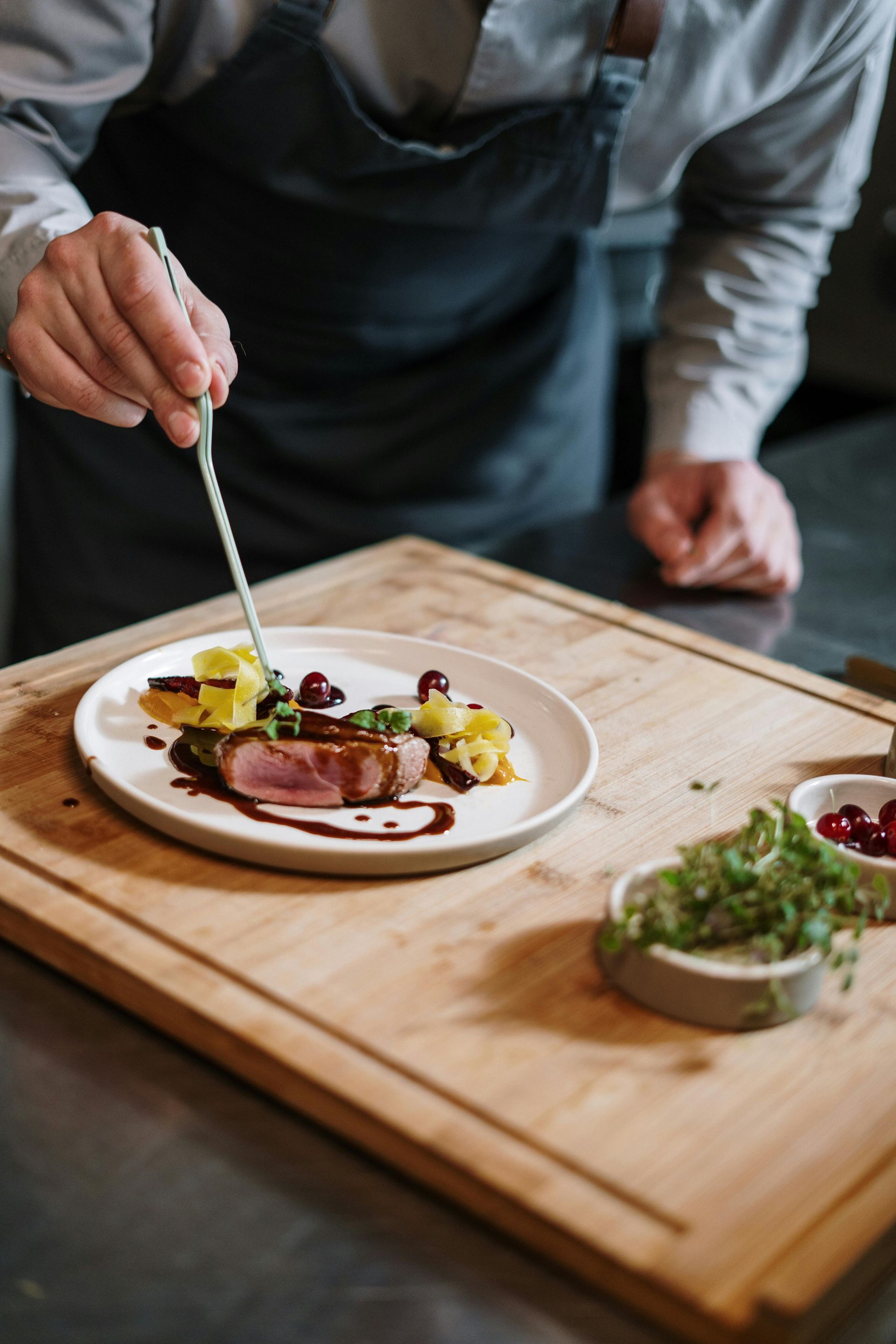 Chef plating a gourmet dish on a wooden board, with fresh herbs and sauce.