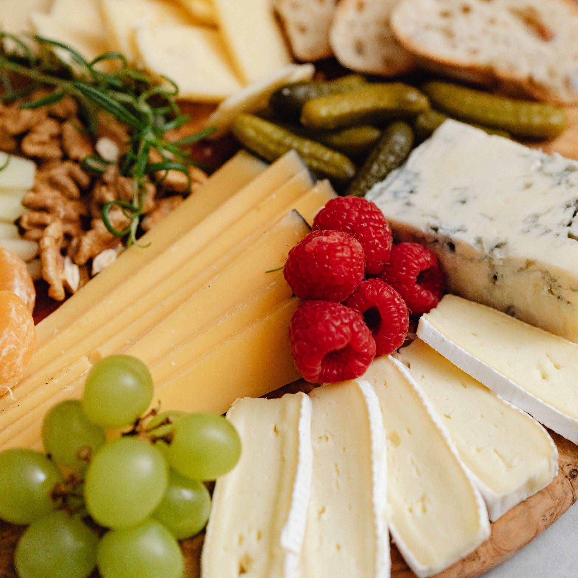 A wooden cutting board topped with cheese , raspberries , grapes and nuts.