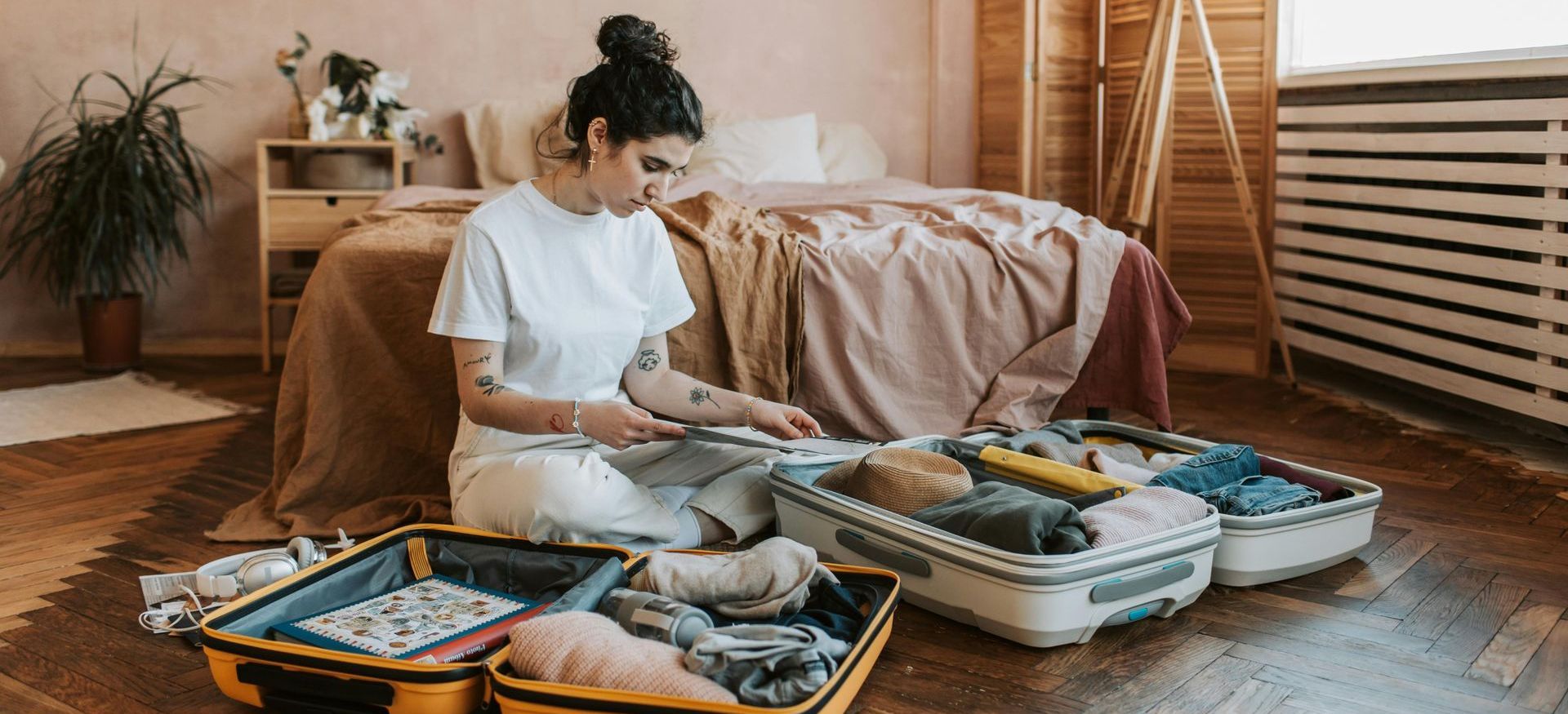 A woman is sitting on the floor packing a suitcase in a bedroom.
