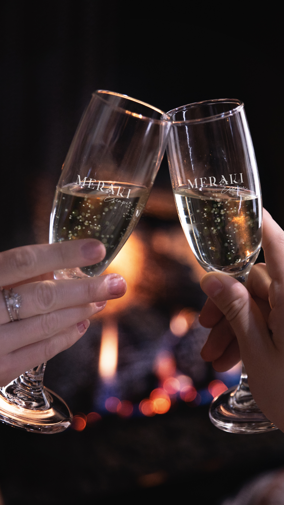 Two hands clinking champagne glasses in front of a fireplace.