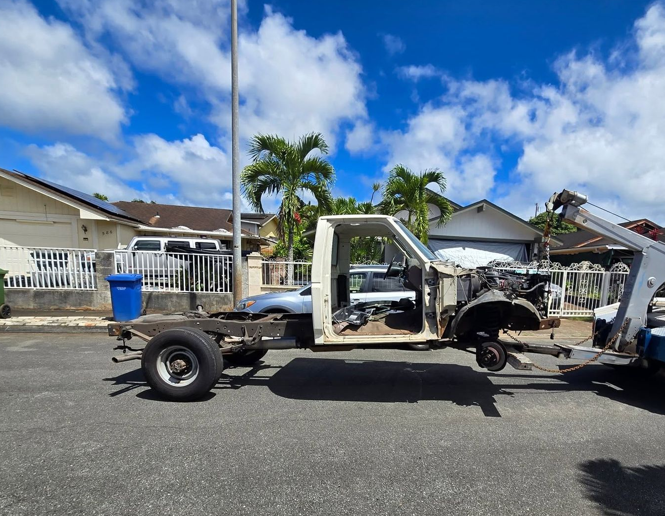 White tow truck hauling a blue pickup on a flatbed beside a road, with a warehouse in the background