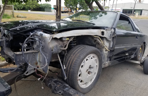 Severely damaged black car with the front end ripped off, parked on a street.