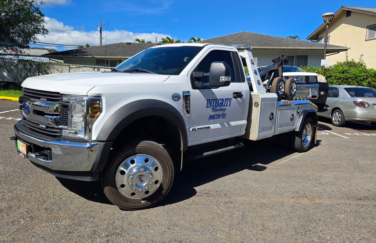 Black pickup truck with blue lettering parked outdoors beside a building, with a trailer attached