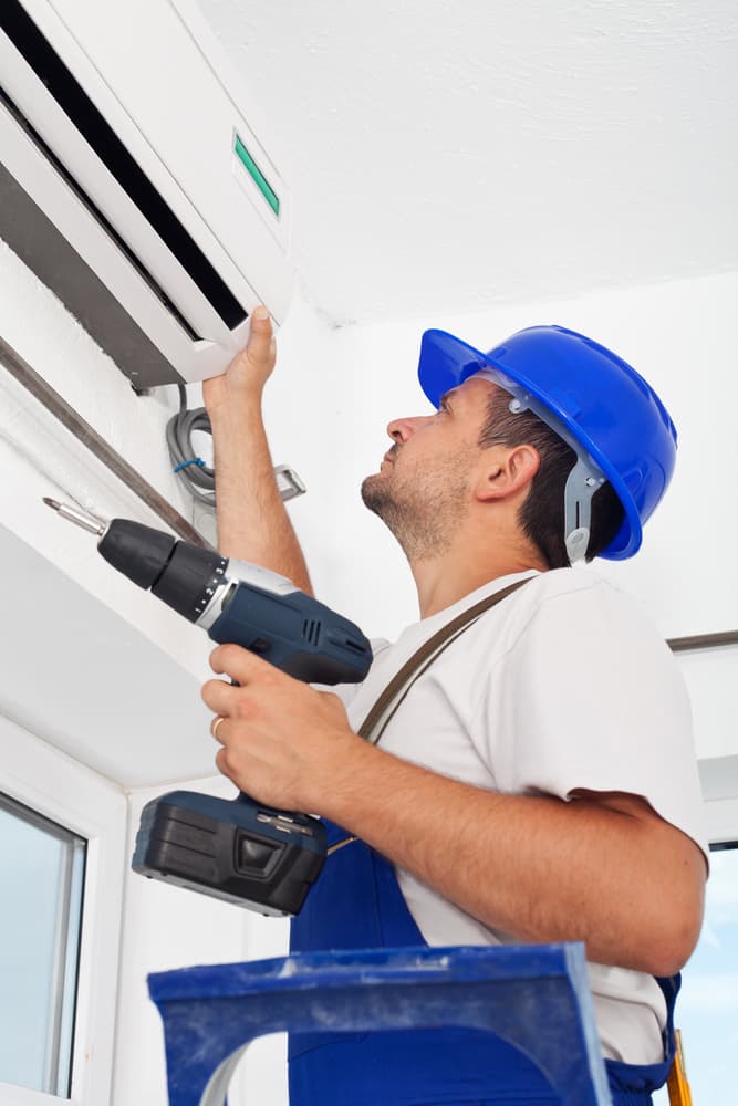A Man is Using a Drill to Fix an Air Conditioner — Action Air N Elec in Forest Glen, QLD