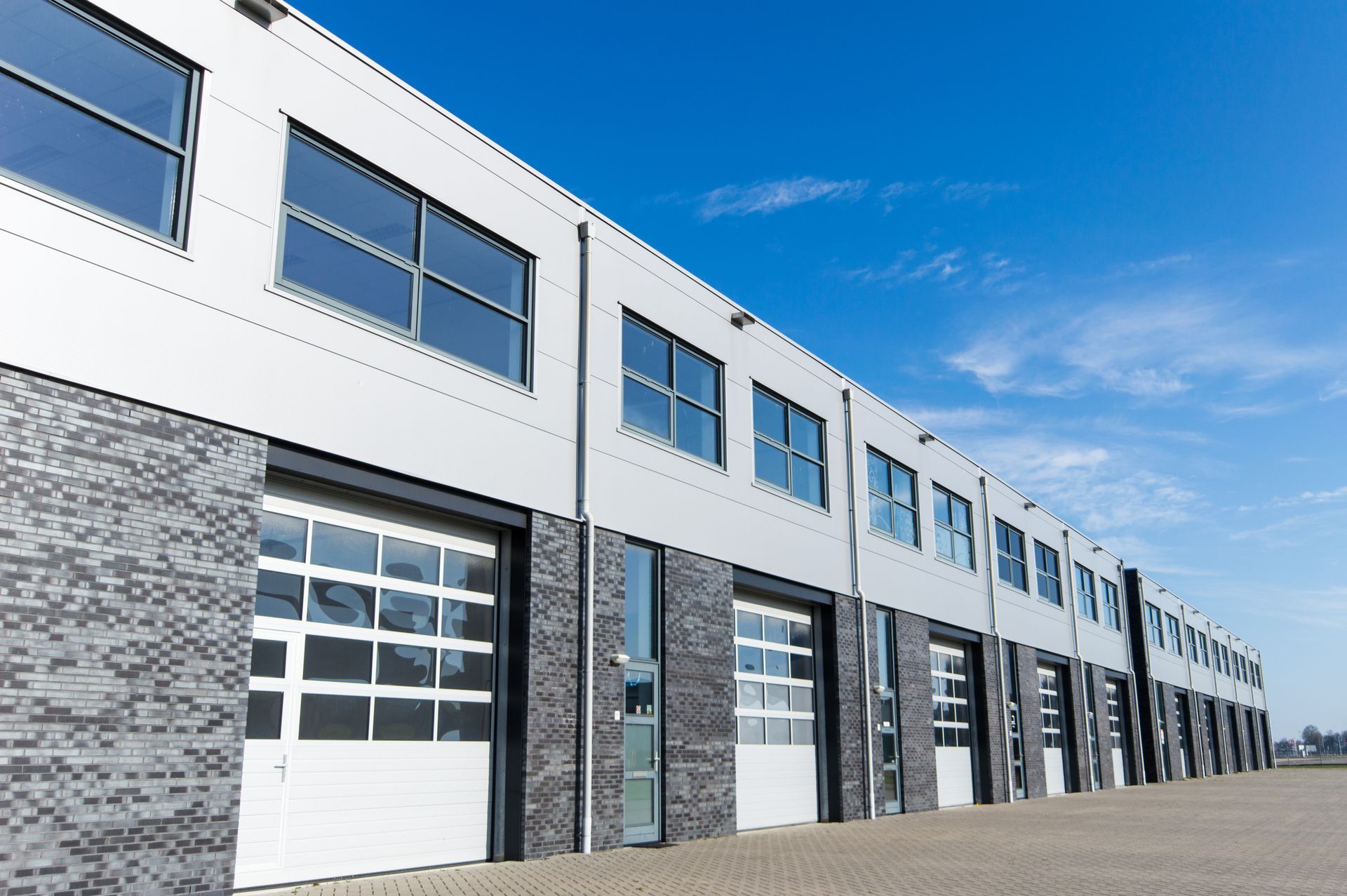 Row of modern industrial units with garage doors and windows, blue sky overhead.
