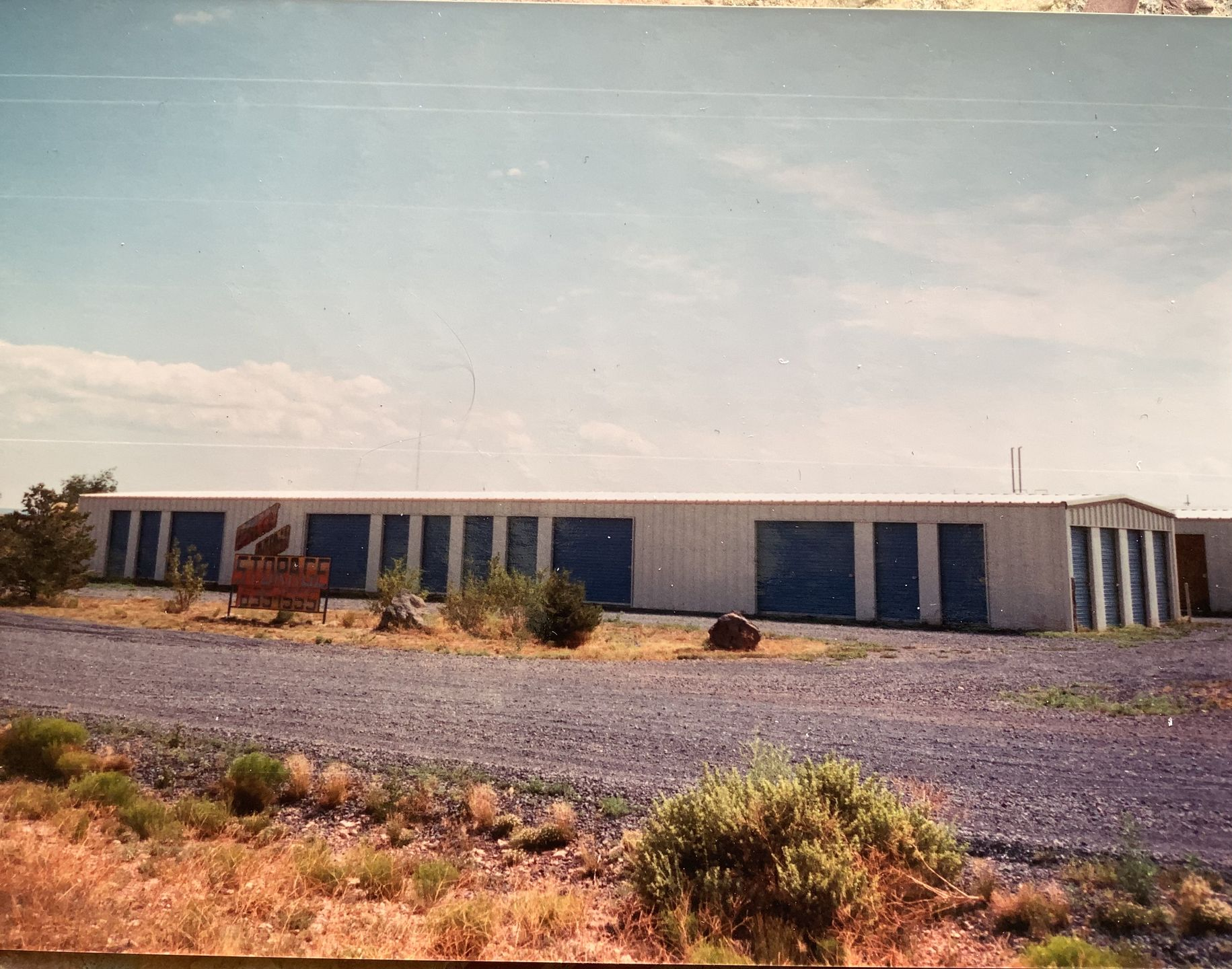 Storage units, one open showing stacked boxes, a second unit closed. A hand truck with boxes stands near the first unit.