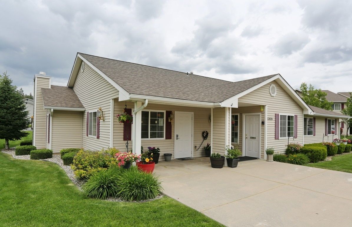 A beige, single-story home with a driveway and landscaping under a cloudy sky.
