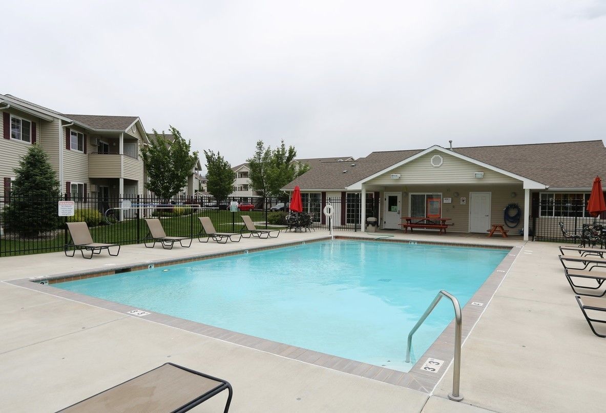 Rectangular pool with blue water, lounge chairs, and apartment building in the background.