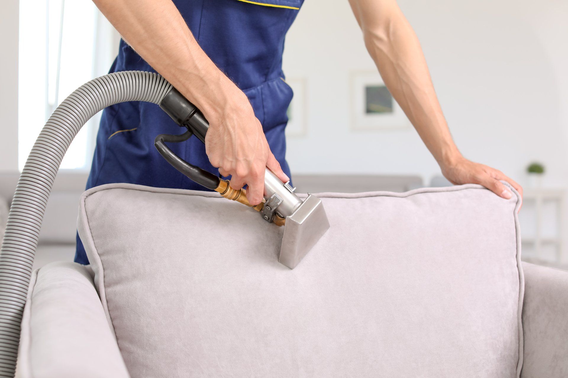 Man janitor in gloves and uniform vacuum clean white carpet with professional equipment